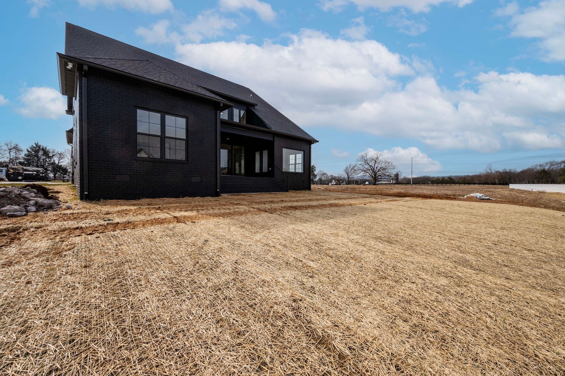 Black house with angled roof on a field of dry grass under a cloudy sky.