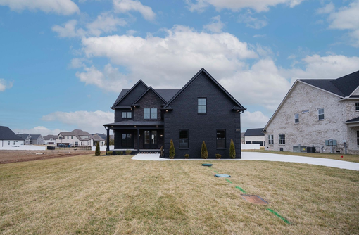 Black brick house with front porch and small yard on a cloudy day.