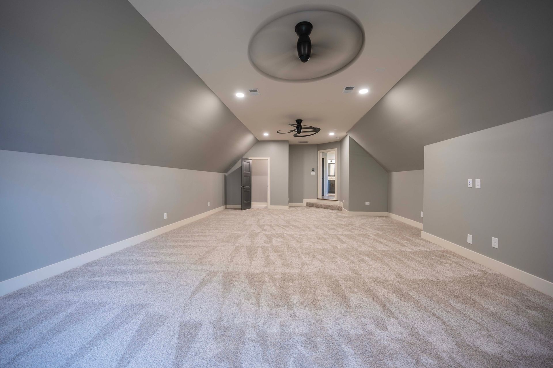 Spacious room with sloped ceiling, gray walls, beige carpet, and a ceiling fan.