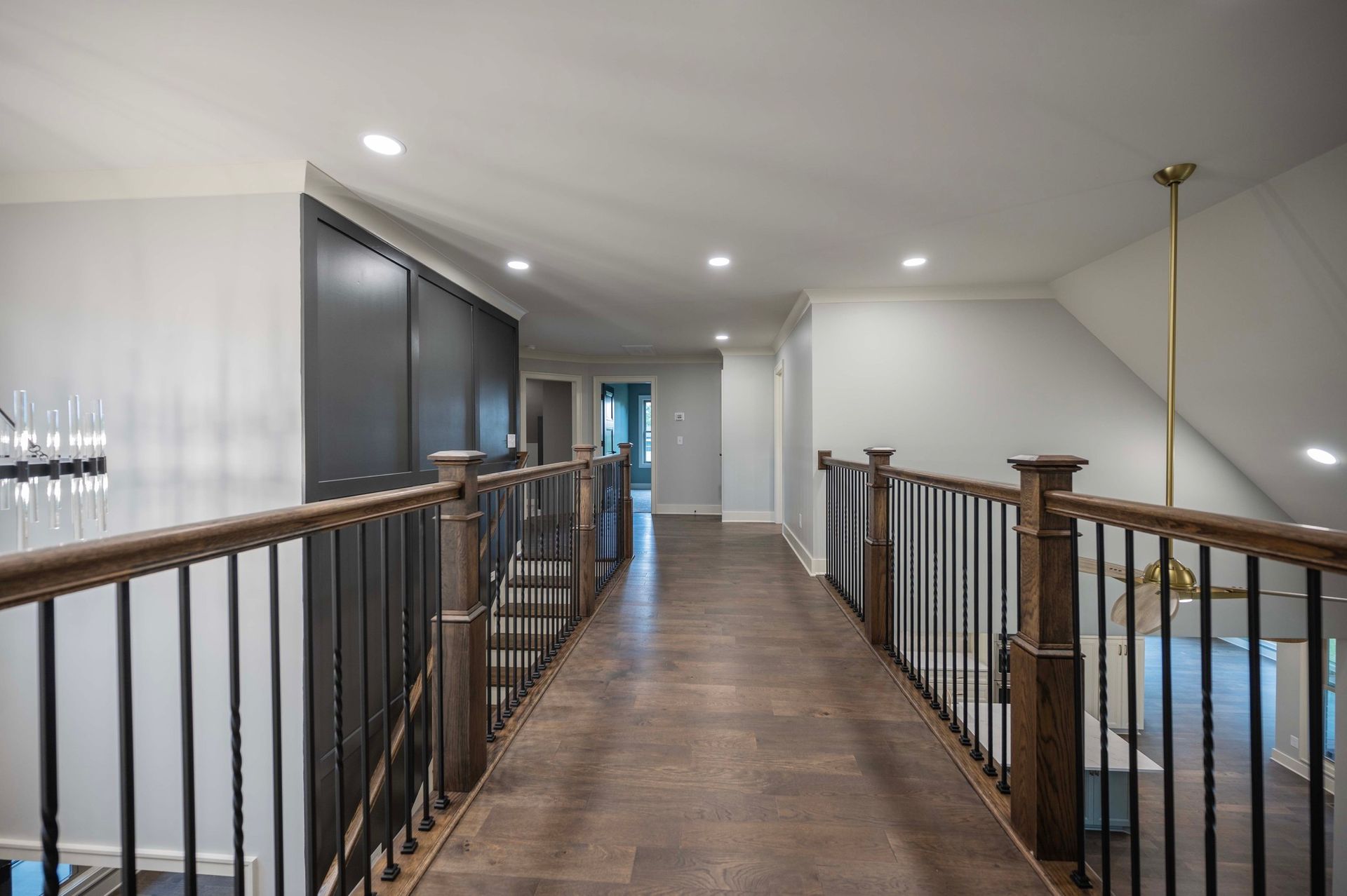 Hallway with dark wood floor, black closet doors, and a wooden and black iron railing.