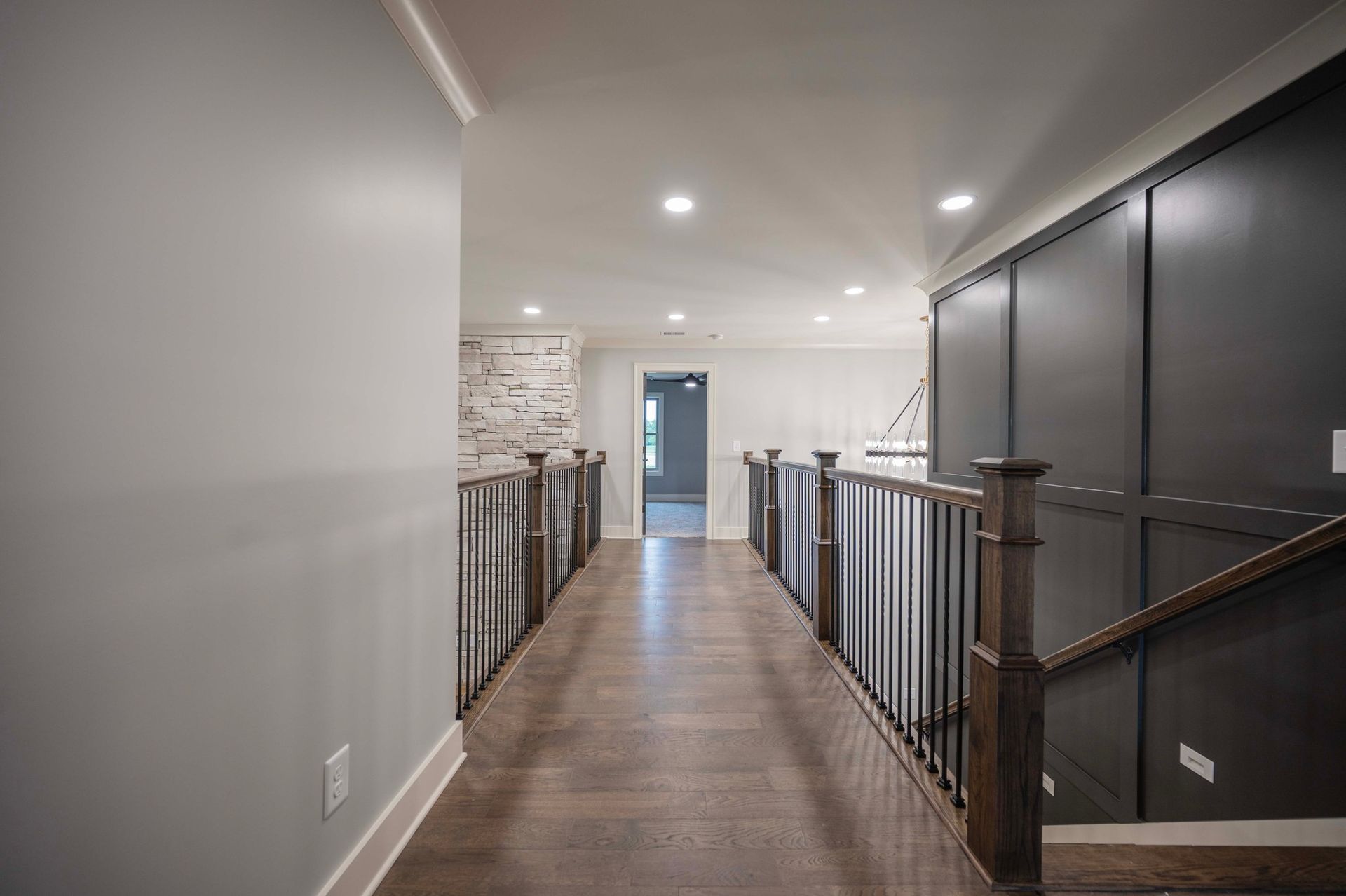 Hallway with wood floor, dark wall paneling, and a brick accent wall. Staircase with wooden railing.