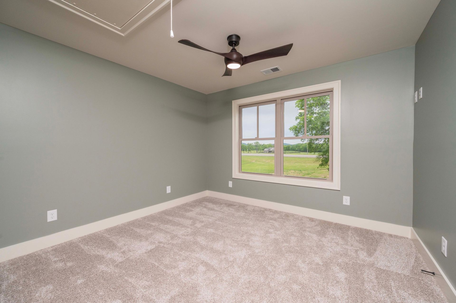 Empty room with gray-green walls, beige carpet, window, and ceiling fan.