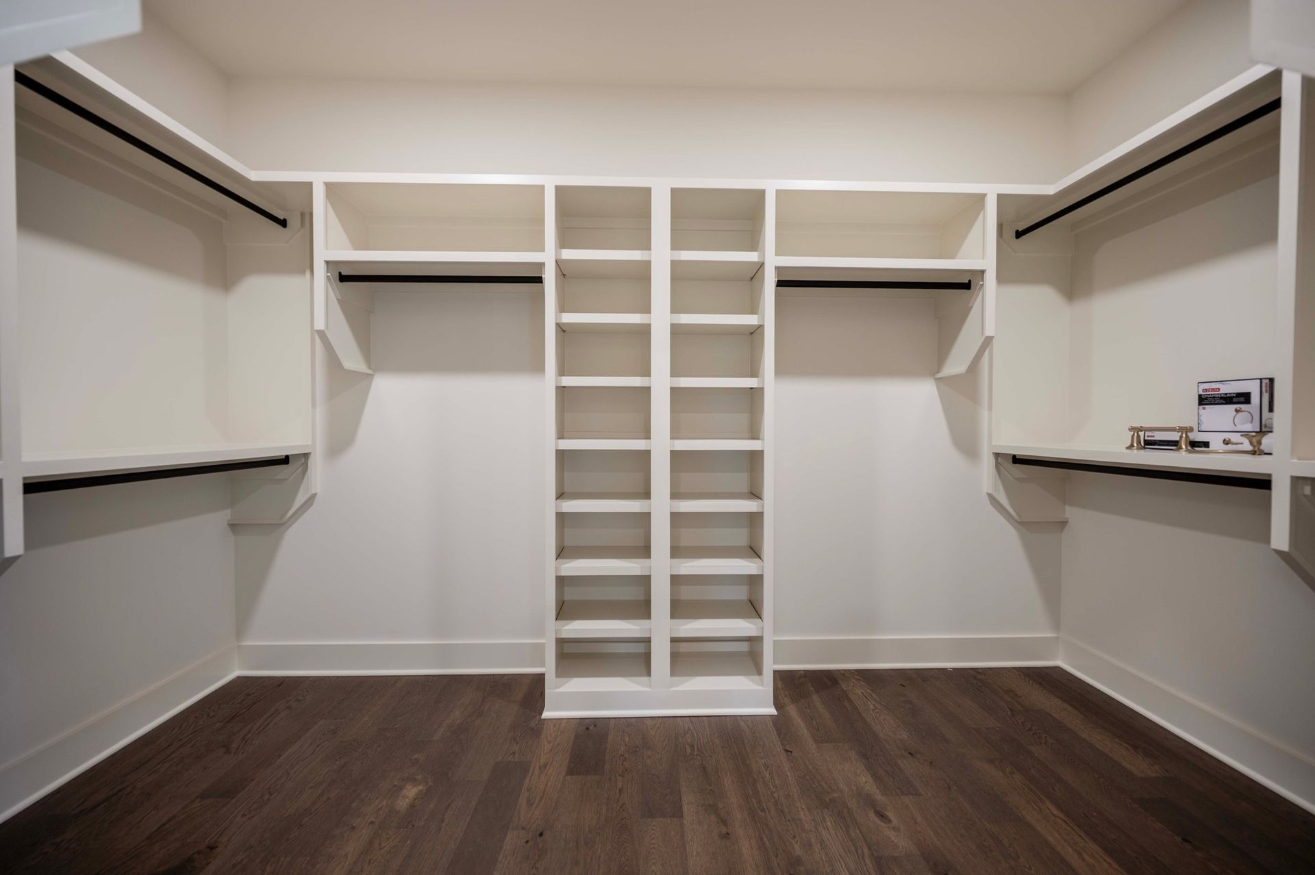 Empty walk-in closet with white shelves, hanging rods, and dark wood floor.