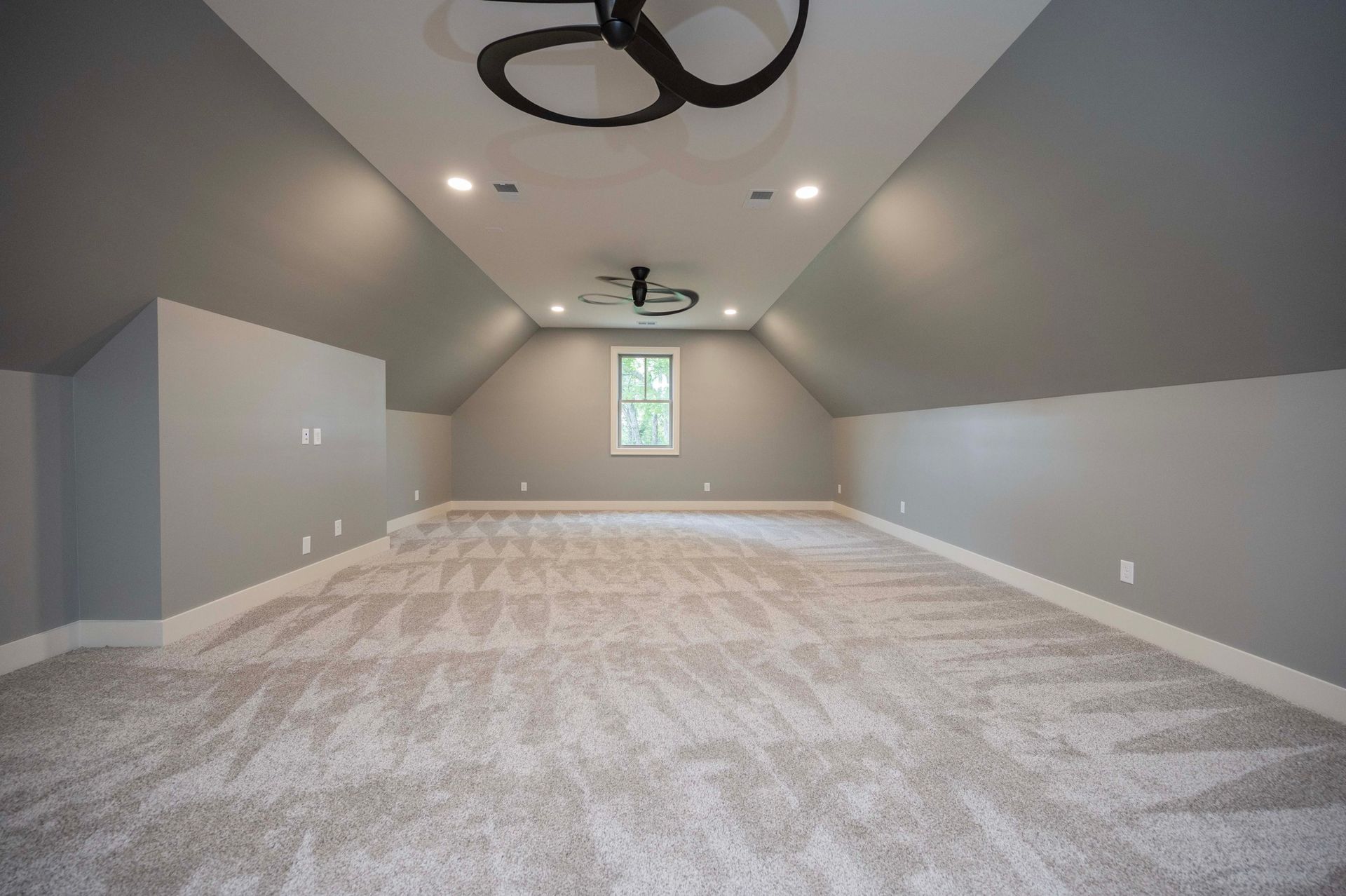 Empty room with gray walls and carpet, window, and two ceiling fans.