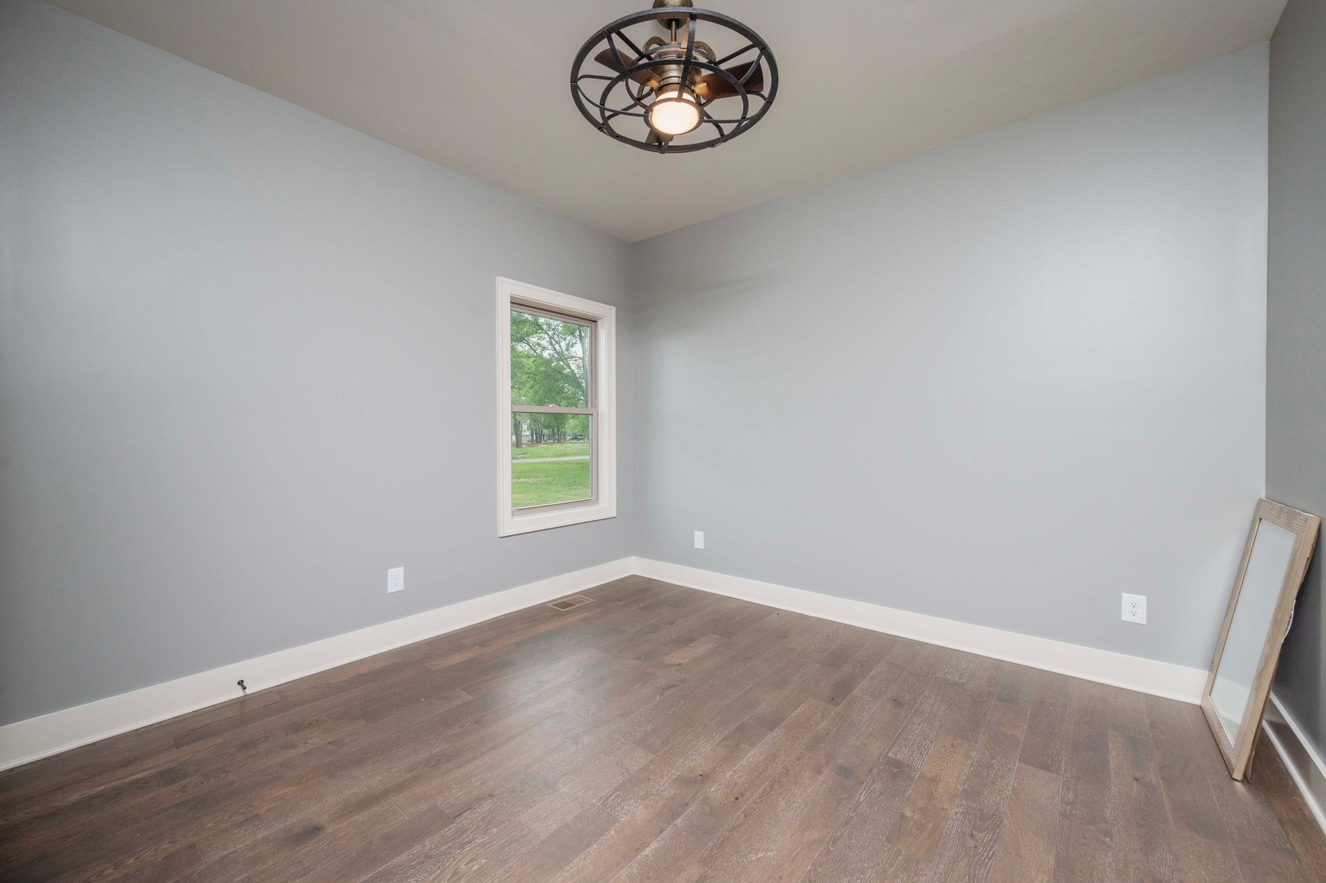 Empty room with gray walls, wood floor, window, and ceiling fan.
