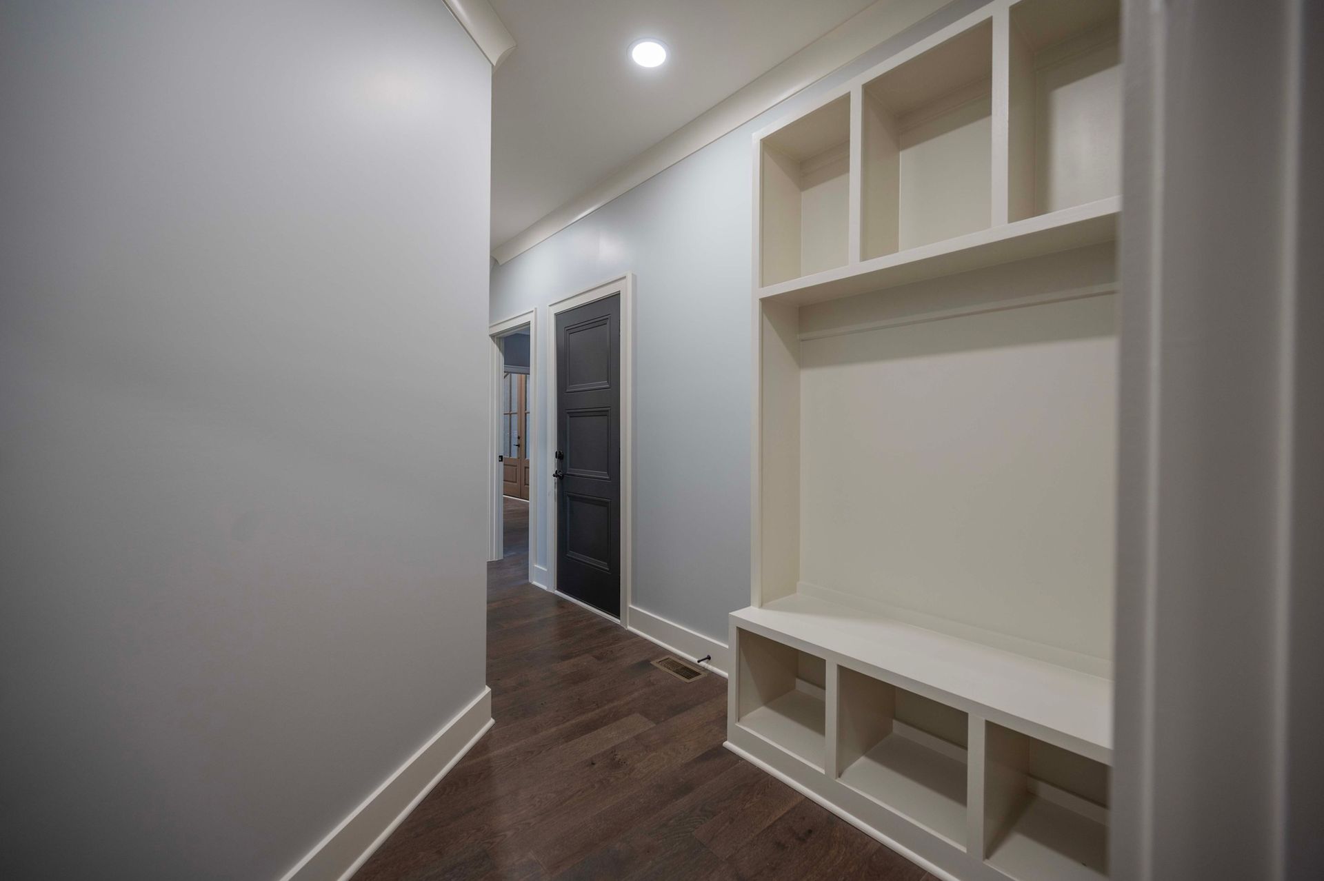 Hallway with built-in white storage unit. Gray walls, dark wood floor, and black door in background.