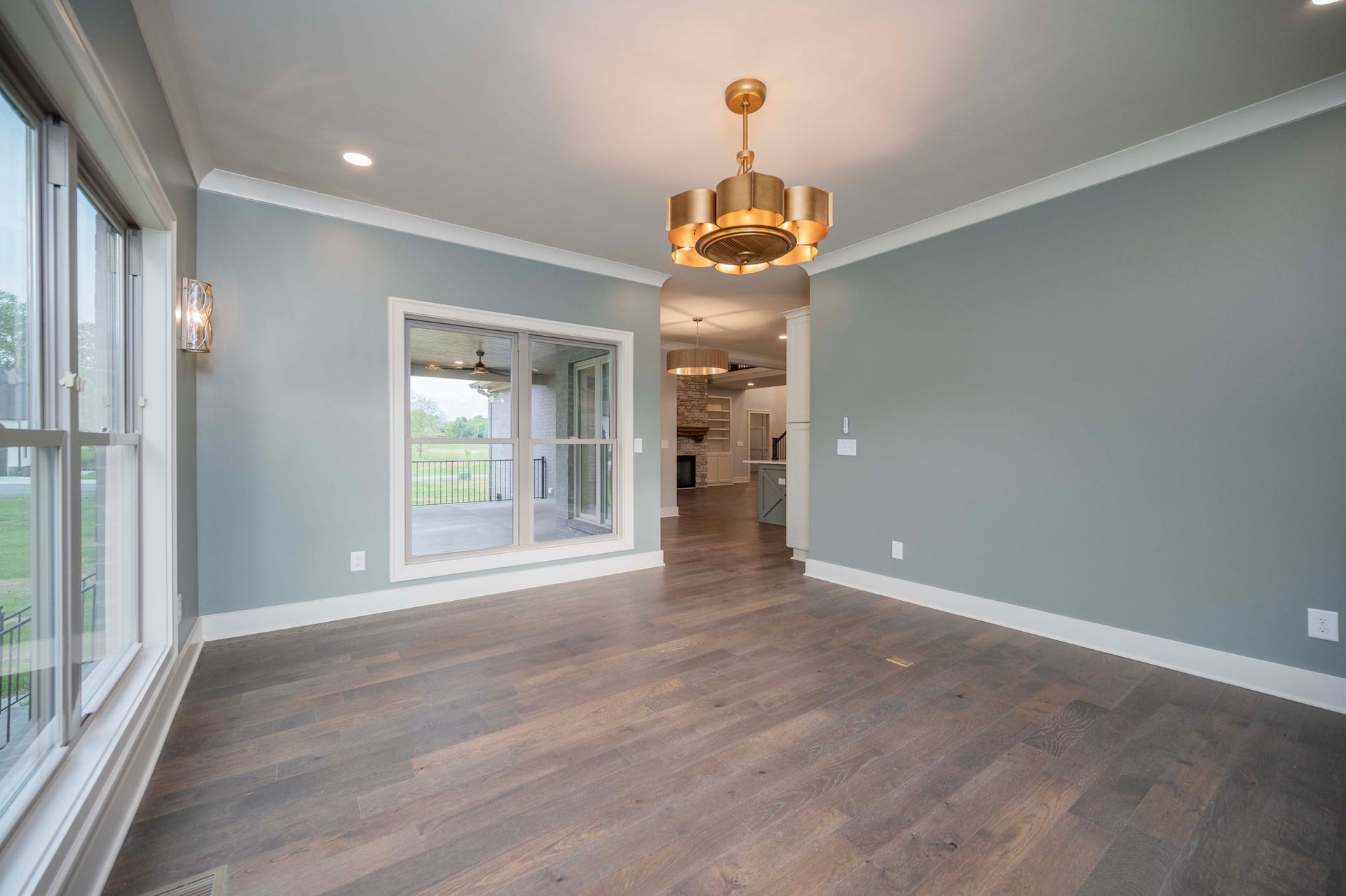 Empty dining room with gray walls, hardwood floors, and gold chandelier.