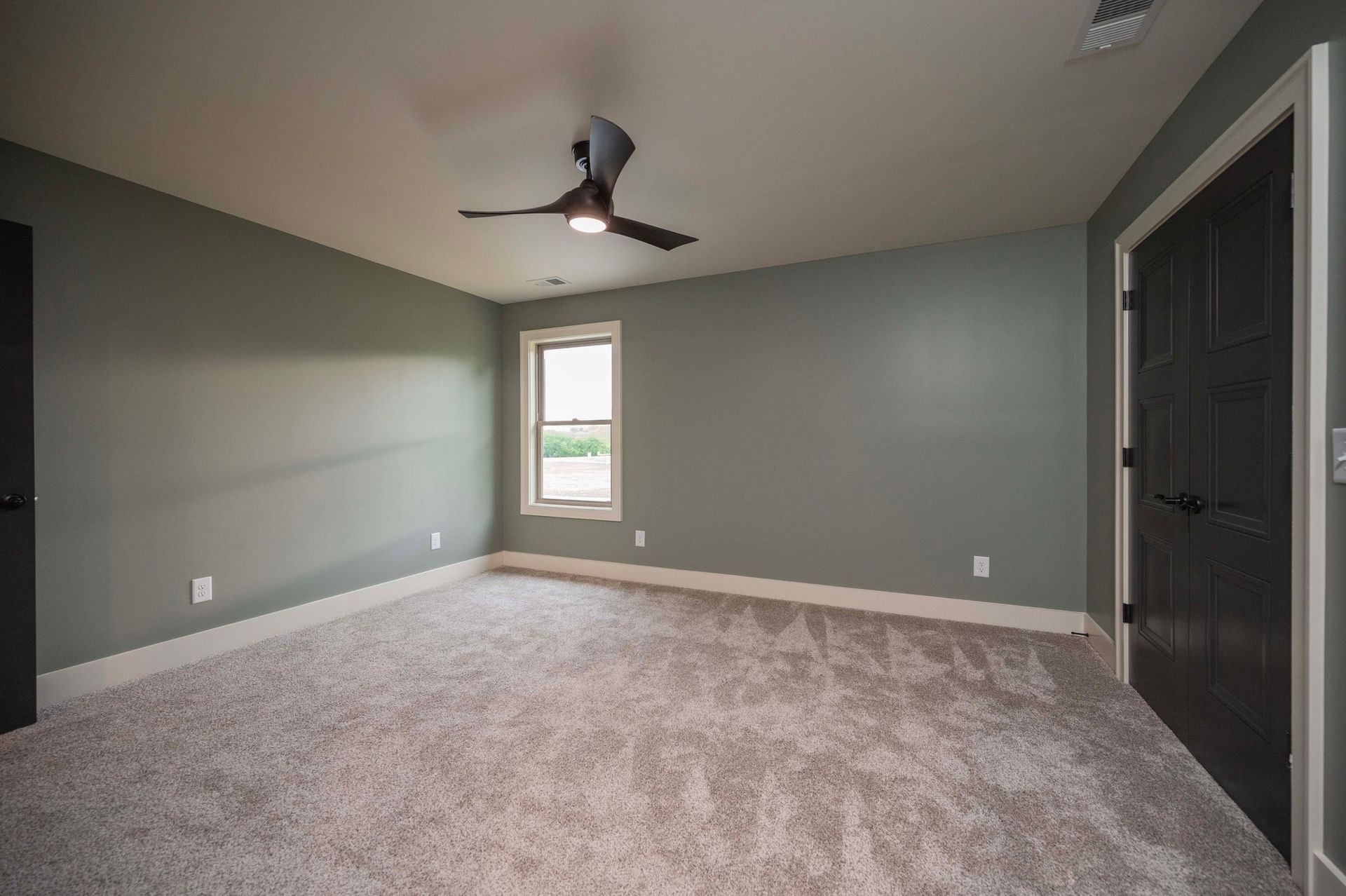 Empty bedroom with gray walls, carpet, ceiling fan, and black doors.