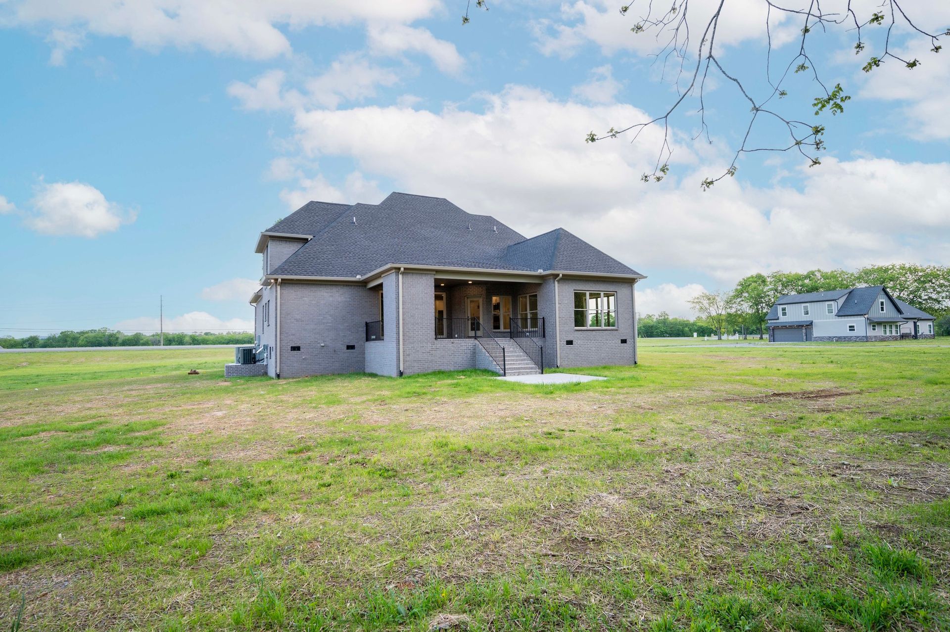 Back of a two-story brick house on a grassy field under a blue sky.
