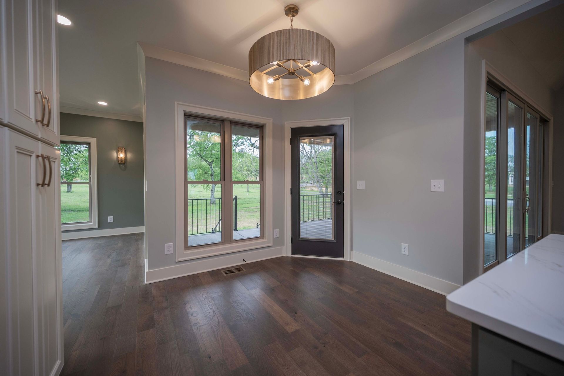 Dining area with wood floor, large windows, and a dark door under a chandelier.