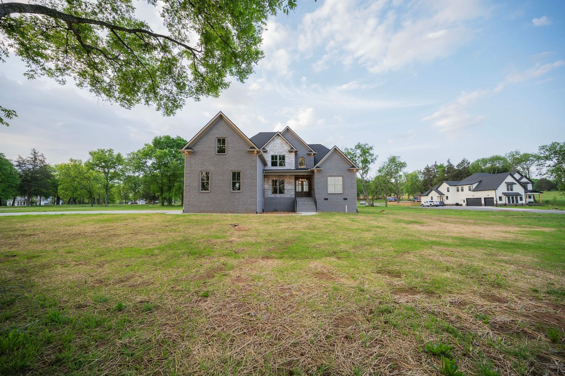 New two-story house under construction, gray brick exterior, in a grassy field on a sunny day.