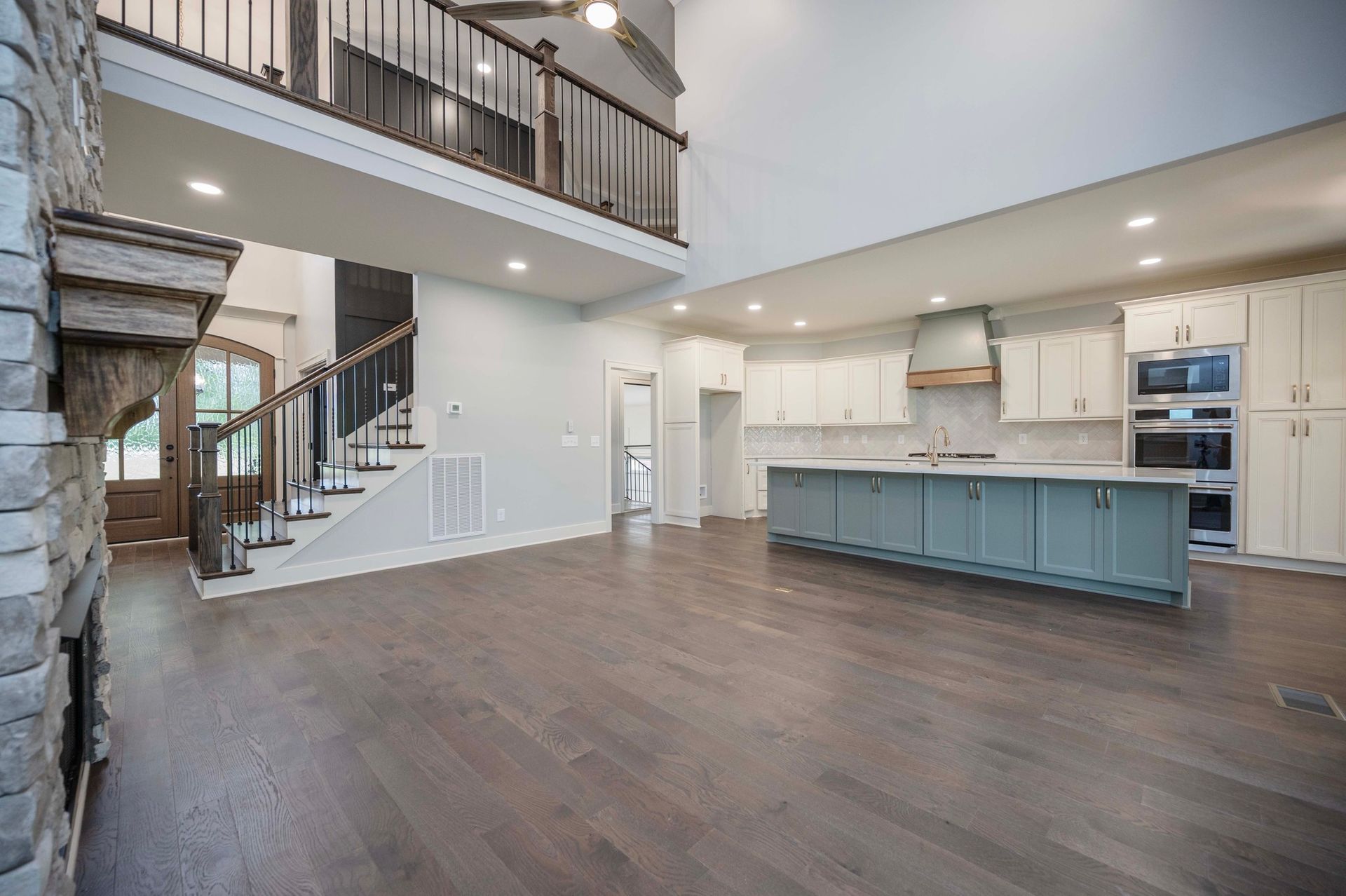 Open-concept living space with a kitchen featuring a teal island, stairs, and a stone fireplace.