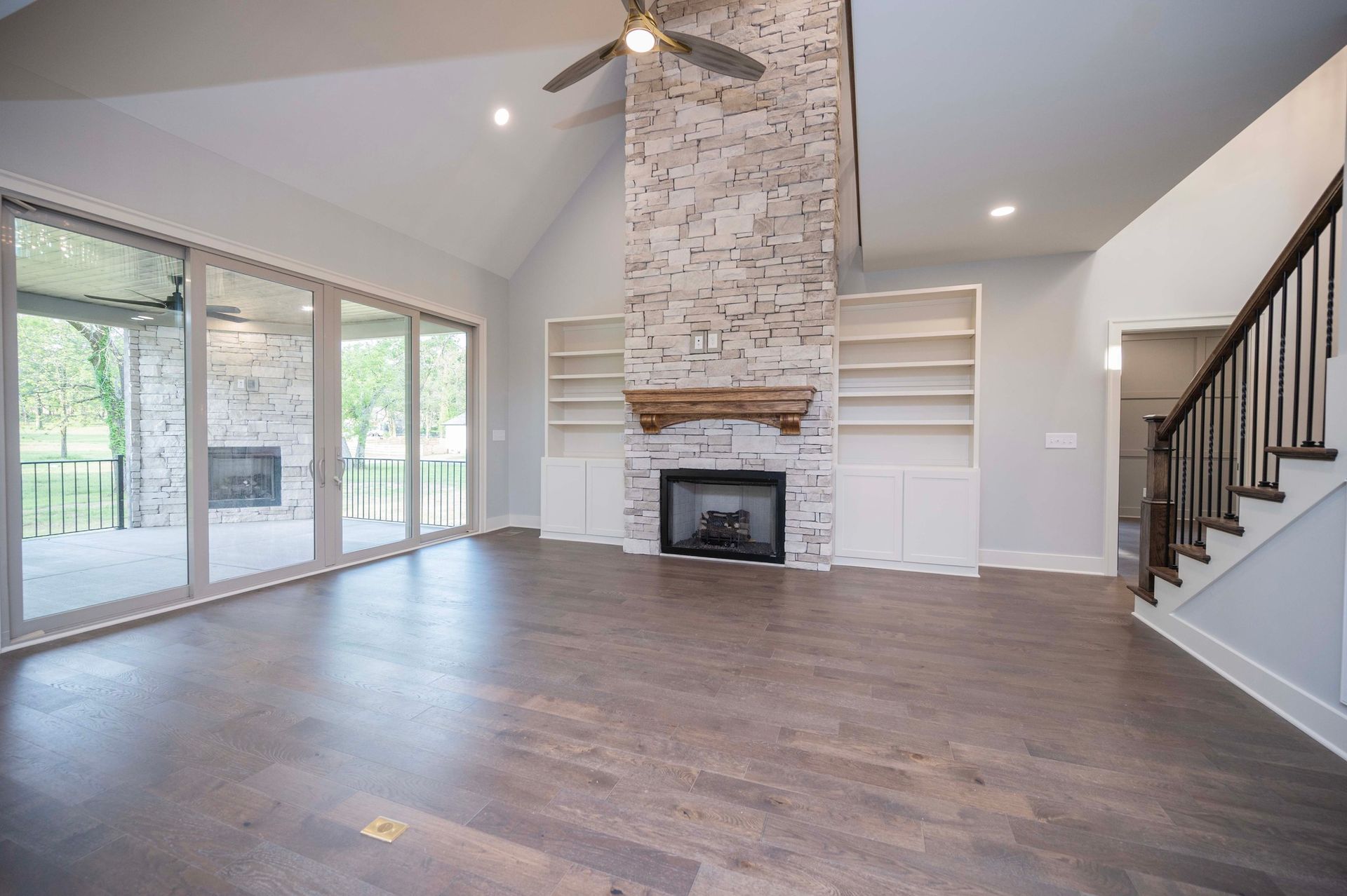 Spacious living room with fireplace, built-in shelves, large windows, and dark wood floors.