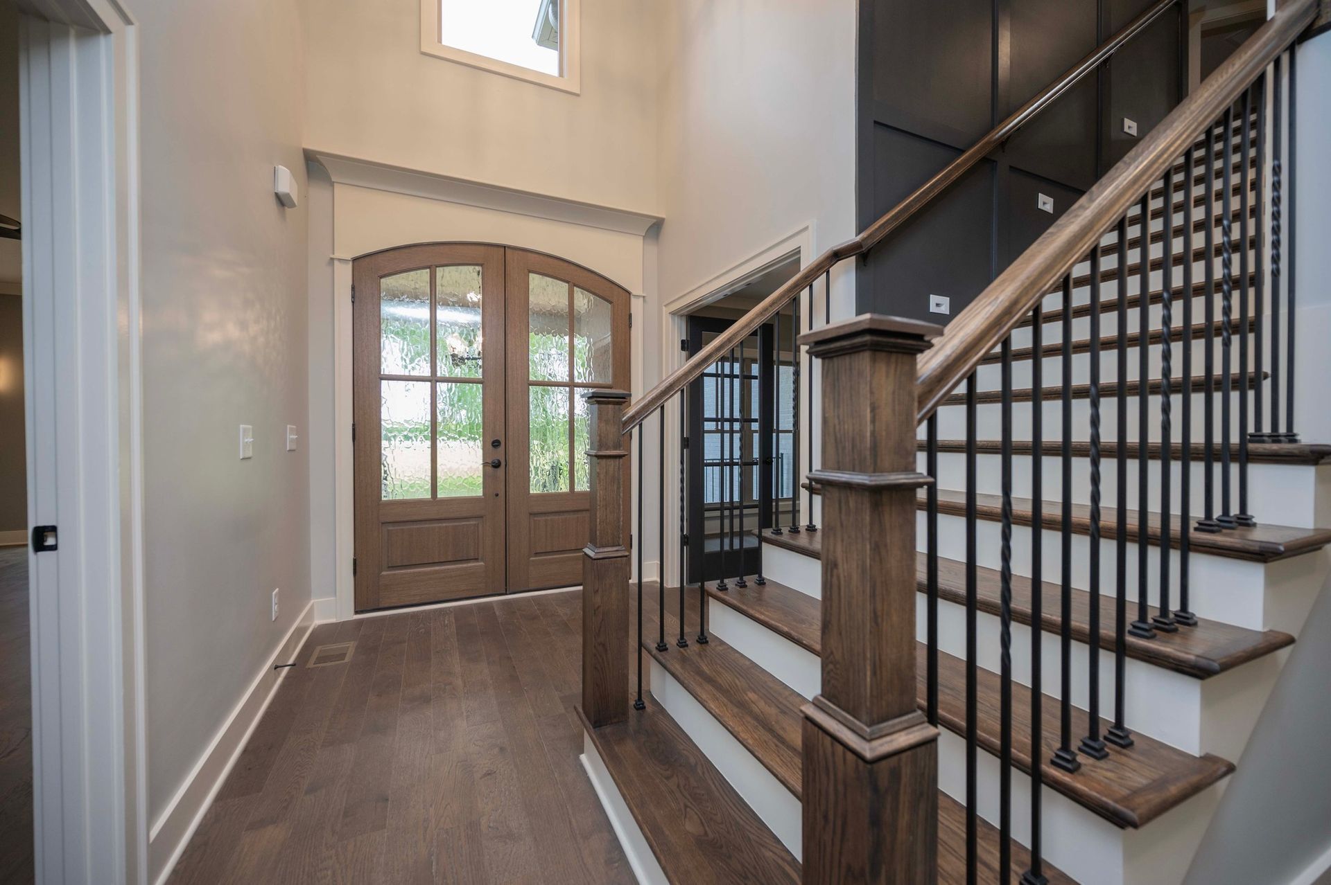 Entryway with double doors, staircase with black iron railing and dark wood steps.