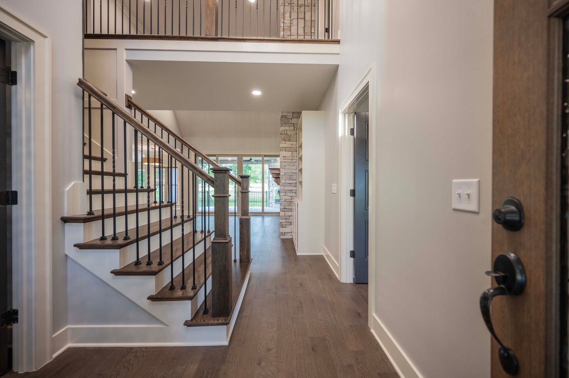 Entryway with staircase, dark wood floors, and white walls. Metal railing, interior door to the right.