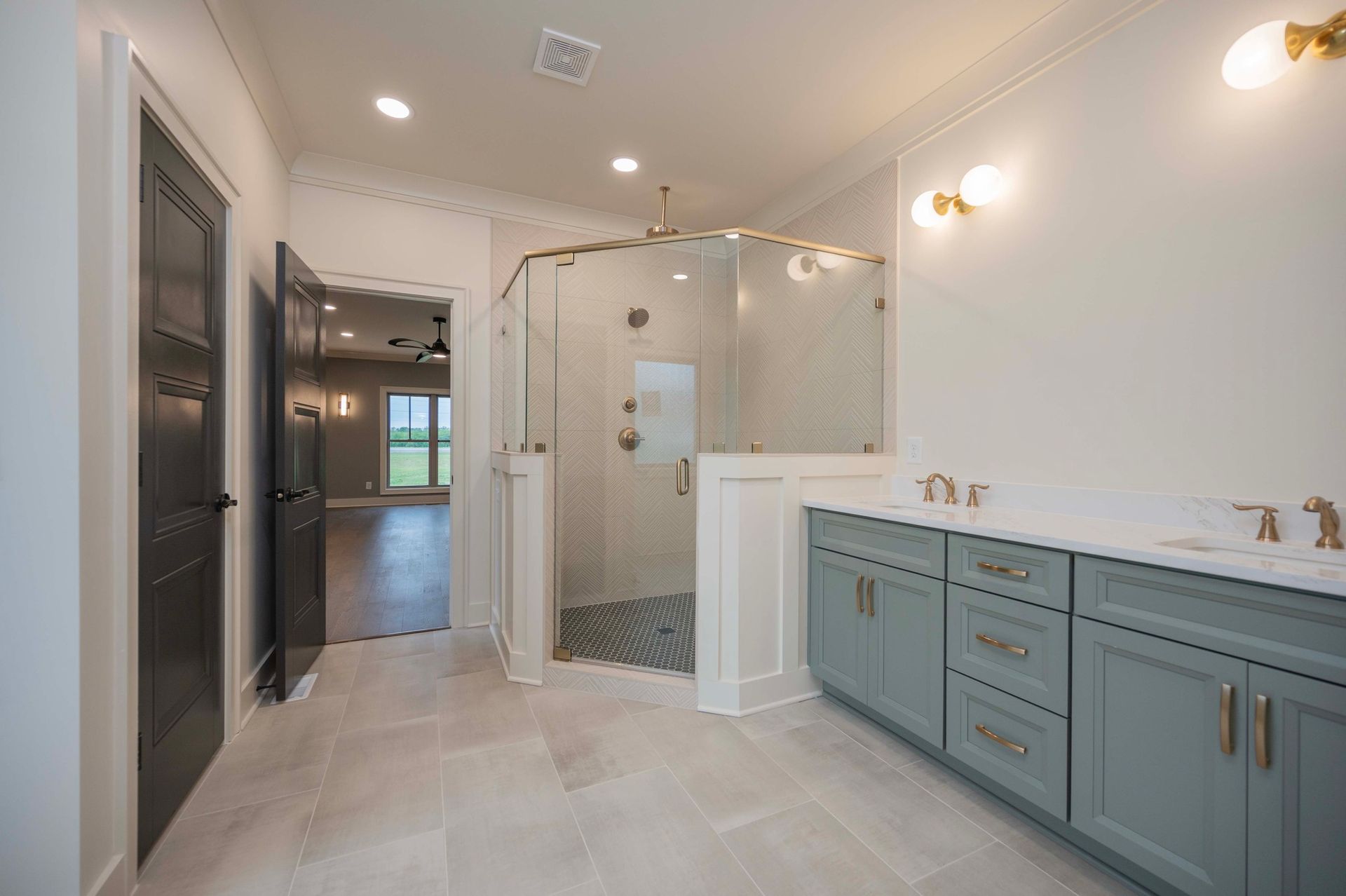 Bathroom with shower, double vanity, and open doorway to another room. Blue cabinets, gold fixtures.
