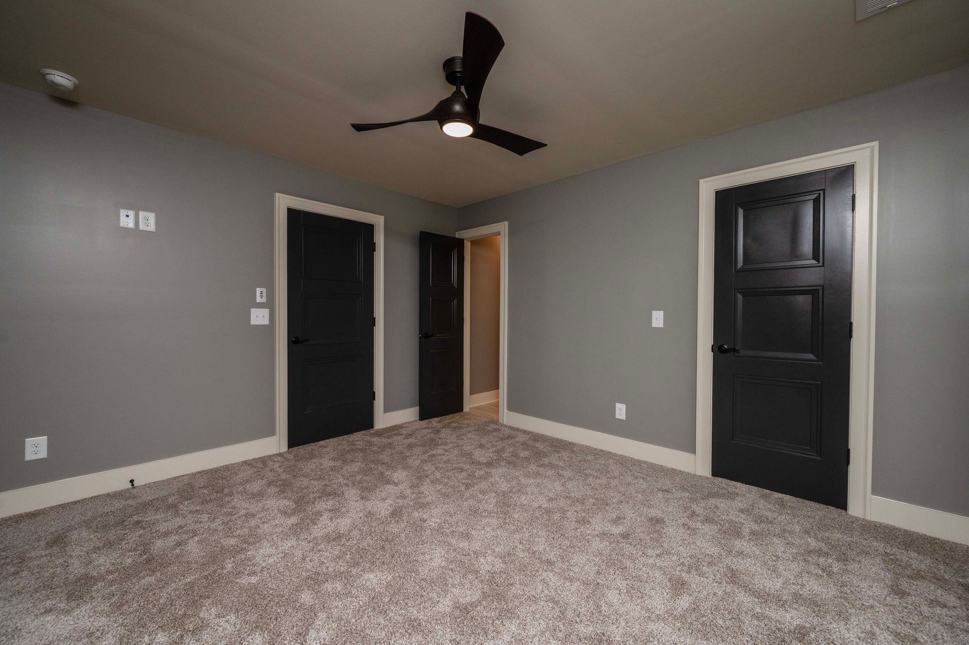 Empty room with gray walls, black doors, brown carpet, and a ceiling fan.