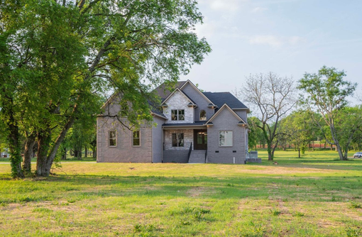 Two-story brick house with white trim, set on a green grassy lawn with trees, under a blue sky.