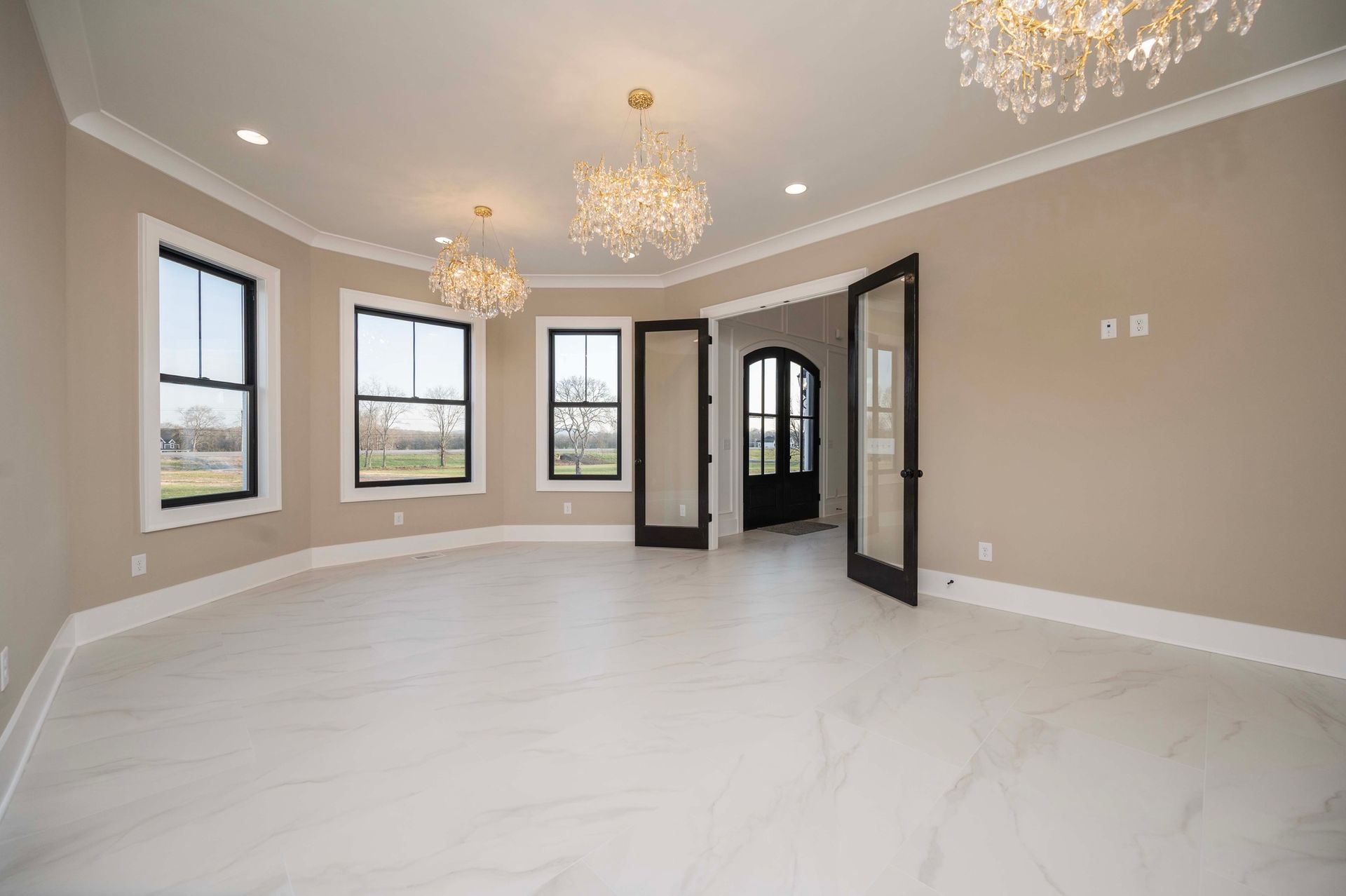 Empty room with white tile floor, beige walls, black-framed windows, and three chandeliers.