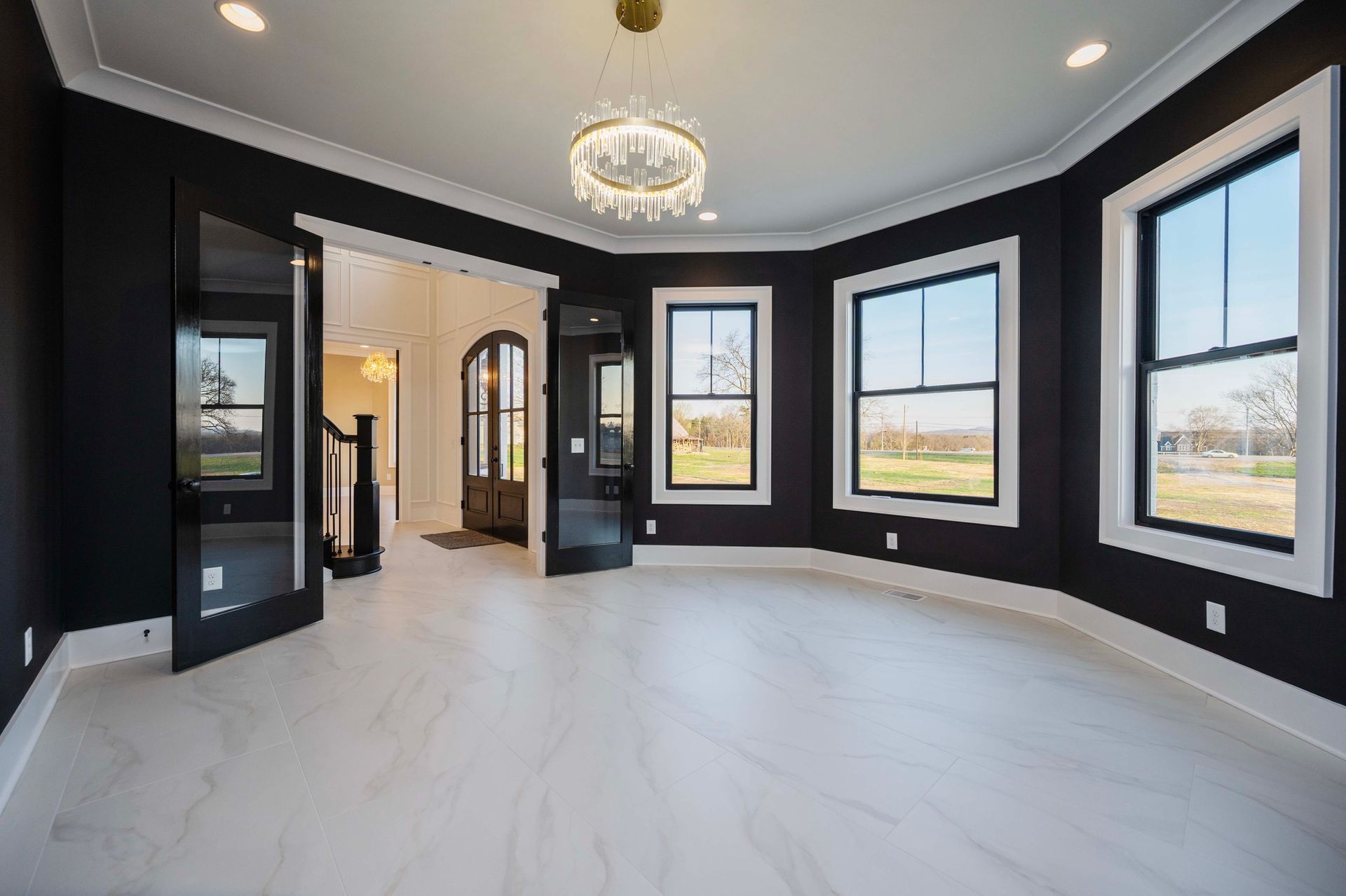 Empty room with black walls, white trim, and a large window.  Crystal chandelier hangs from the ceiling.