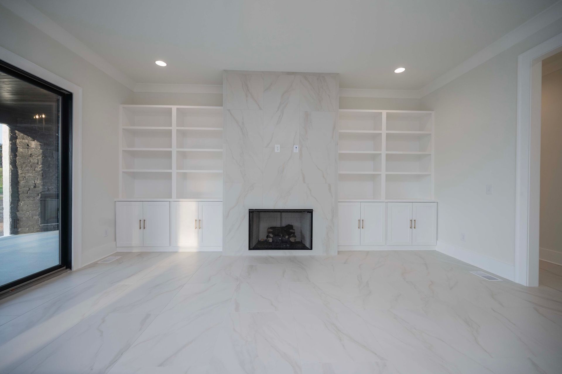 White room with marble fireplace, built-in shelves, and large window.