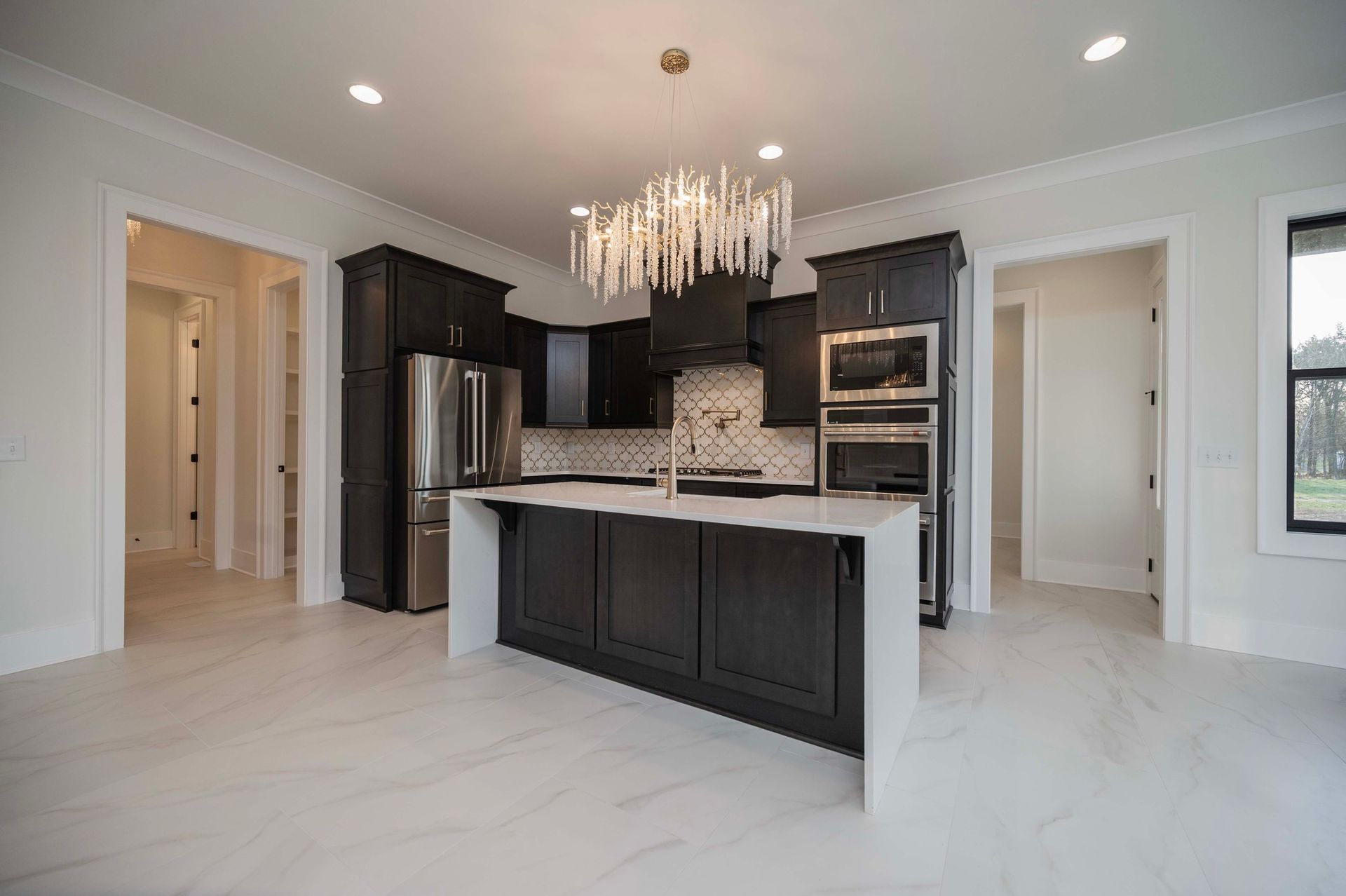 Modern kitchen with dark cabinets, white countertops, and a decorative chandelier.