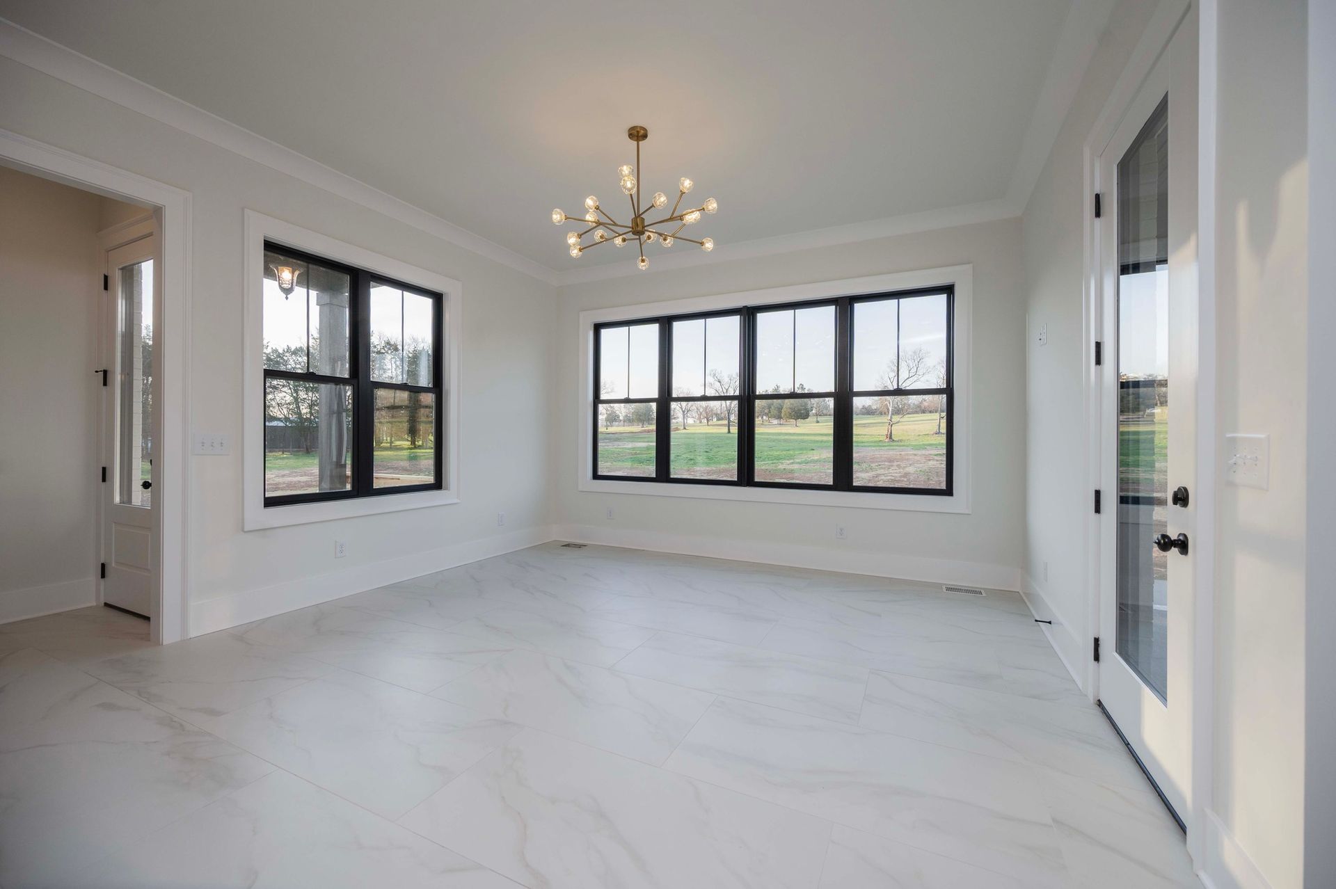 Empty room with large windows, white walls, and a chandelier.