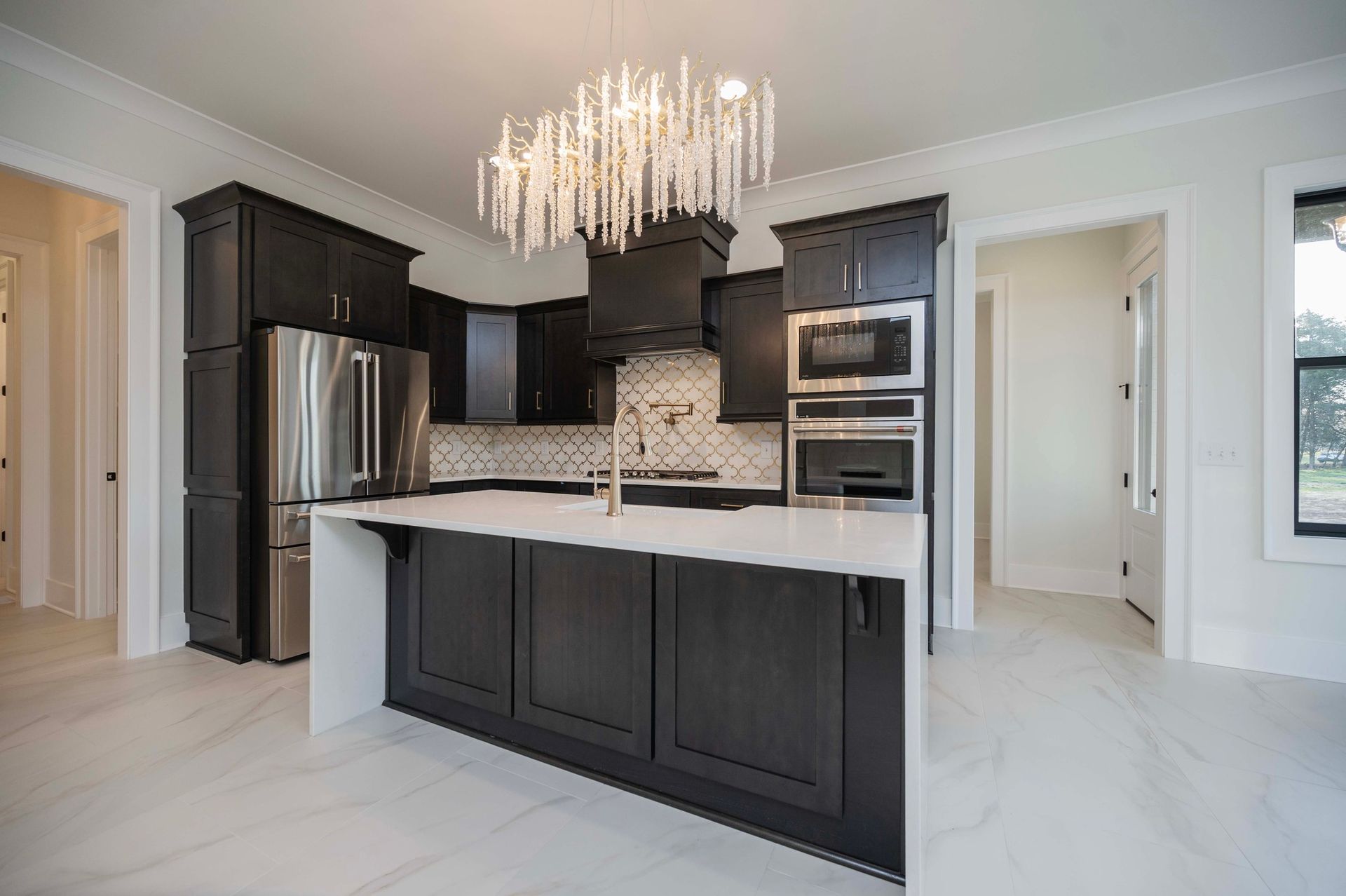 Modern kitchen with dark cabinets, white countertops, island, and chandelier.