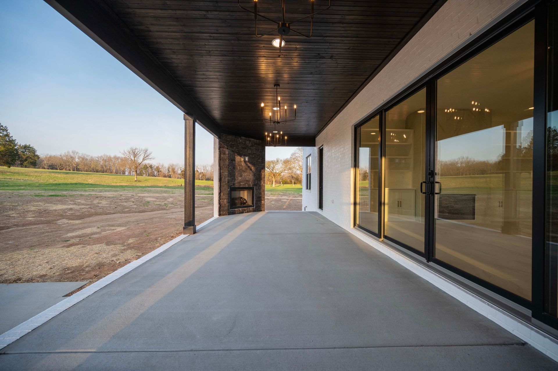 Covered patio with gray concrete, black trim, and large glass doors overlooking a field.