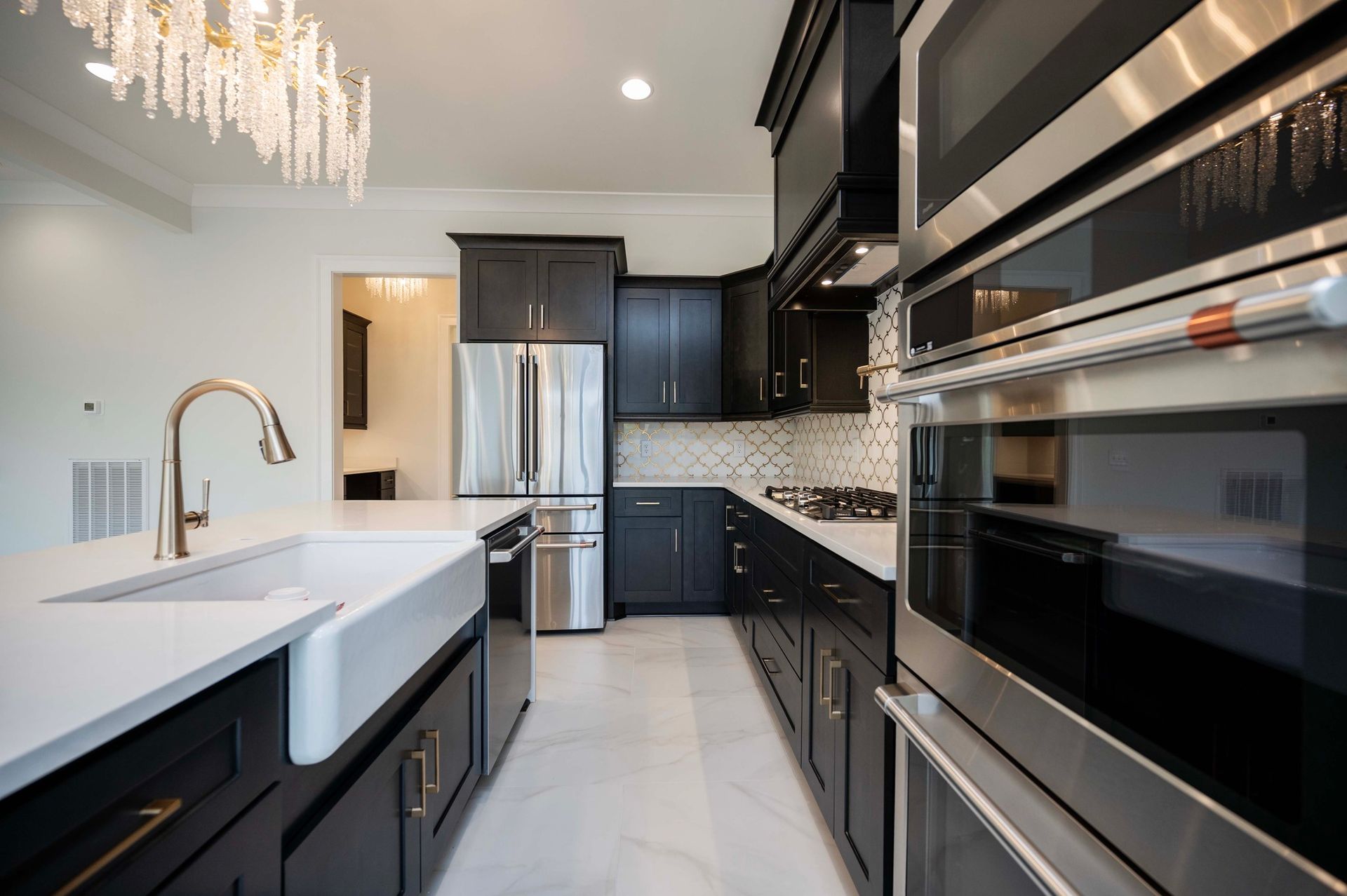 Modern kitchen with black cabinets, white countertops, stainless steel appliances, and a farmhouse sink.