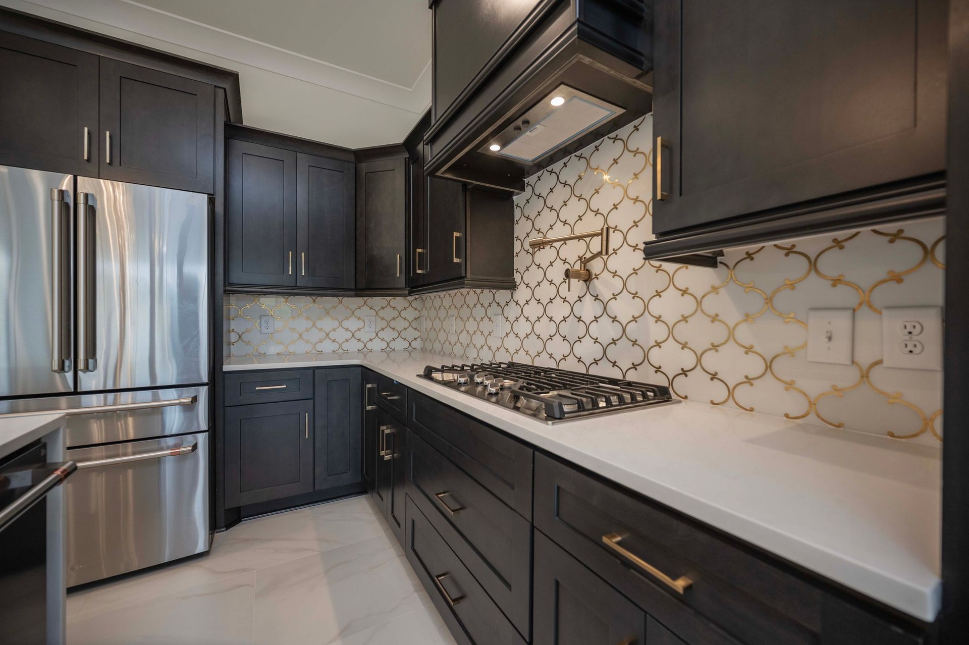 Dark gray kitchen with stainless steel appliances, white countertops, and patterned backsplash.