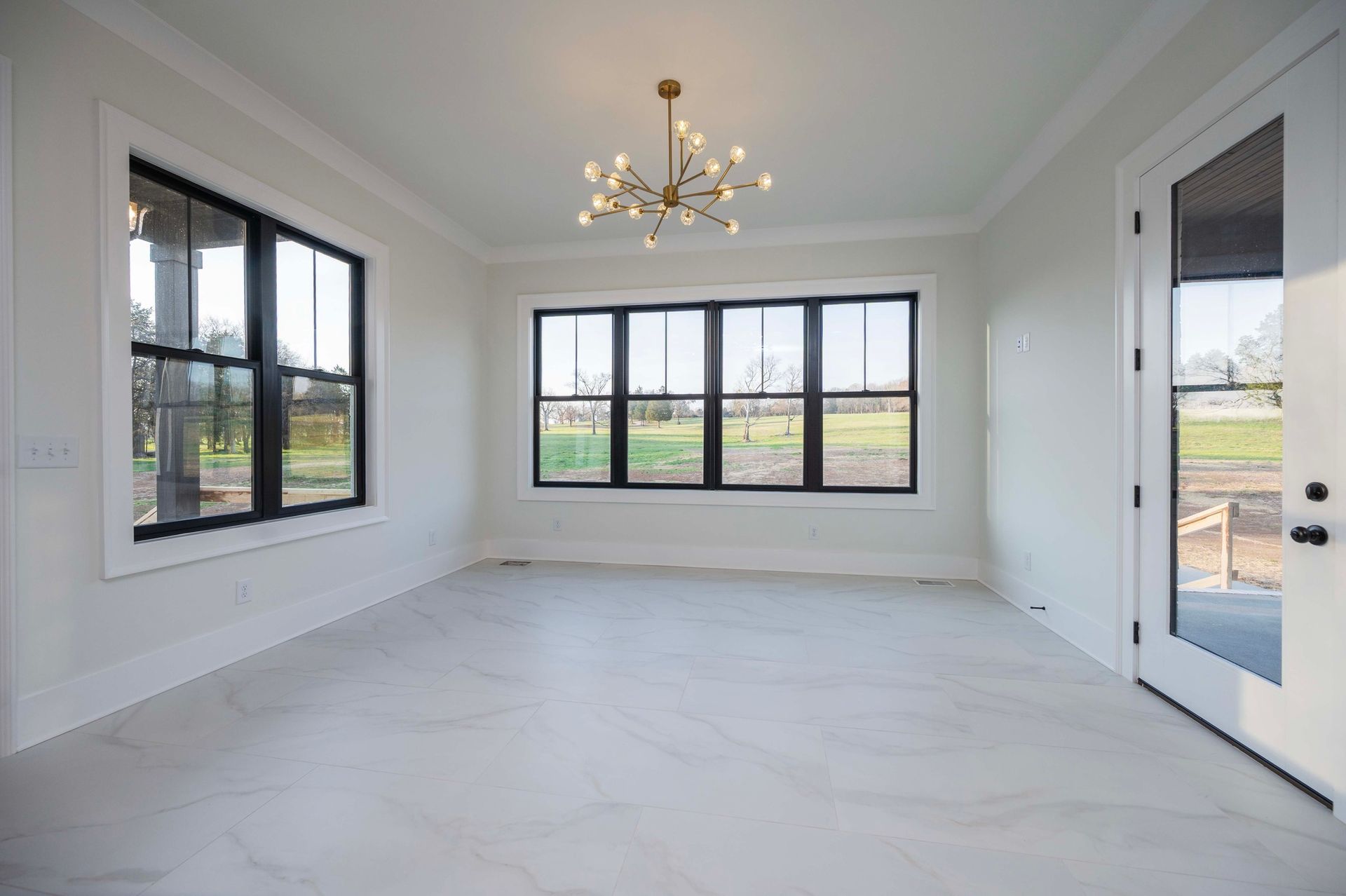 Empty room with white walls, black framed windows, and a gold chandelier.