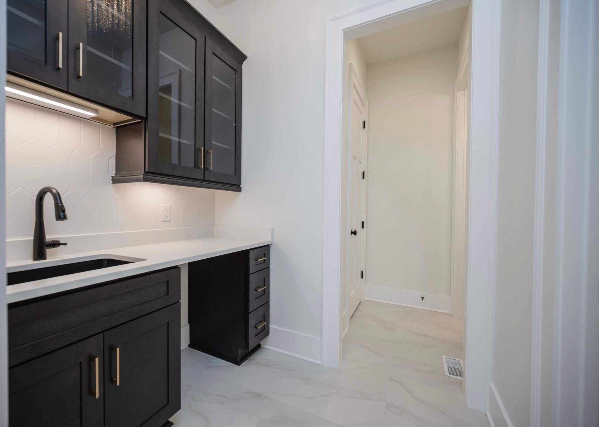 Black cabinets and white countertop in a modern pantry; hallway visible.