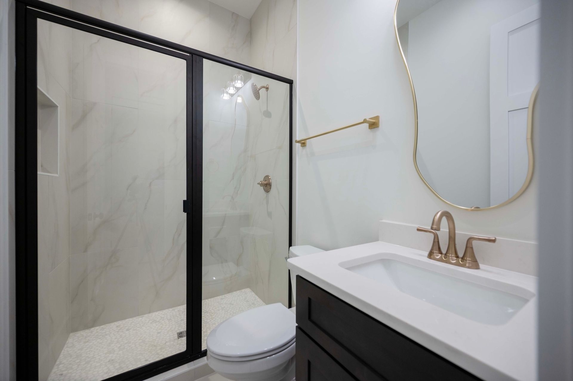 Bathroom with a black-framed shower, white sink, gold accents, and white tile walls.