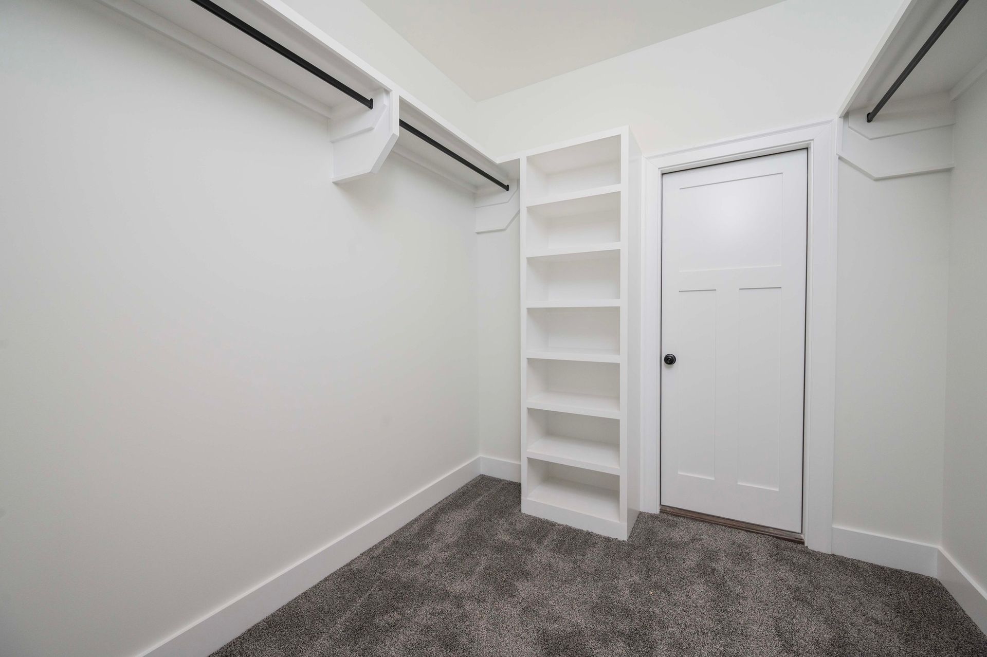 Empty white closet with built-in shelves and a closed door, gray carpet.