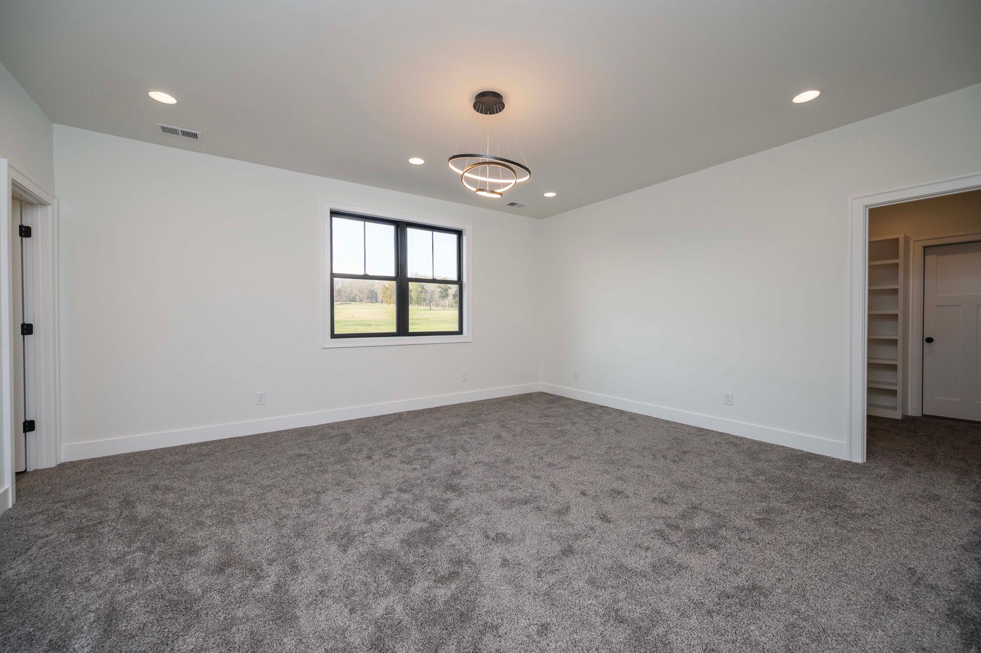 Empty room with gray carpet, white walls, black-framed window, and a modern light fixture.
