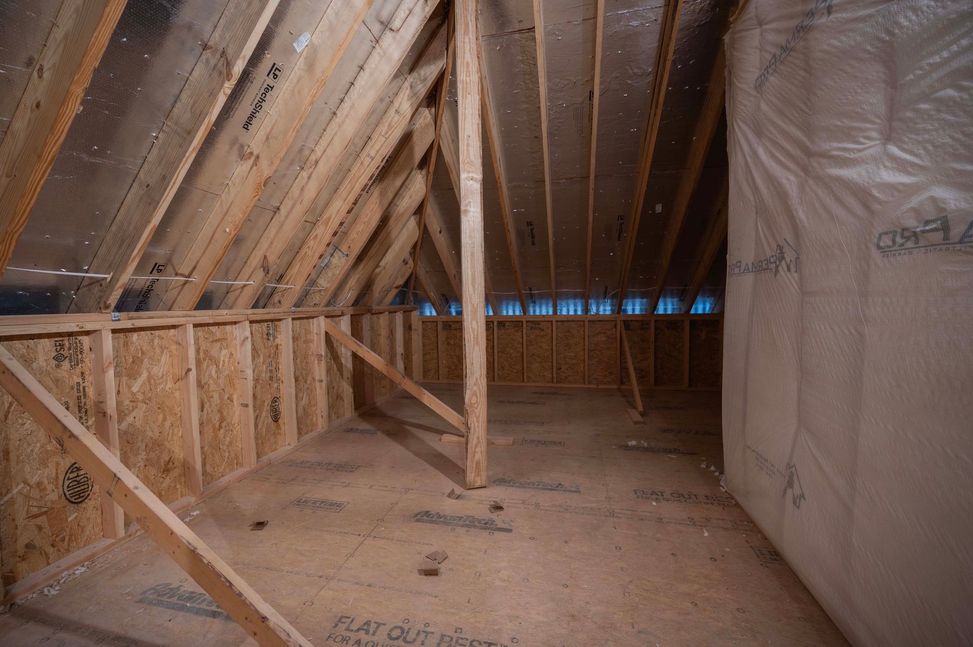 Unfinished attic interior with wooden beams, plywood walls, and insulation.
