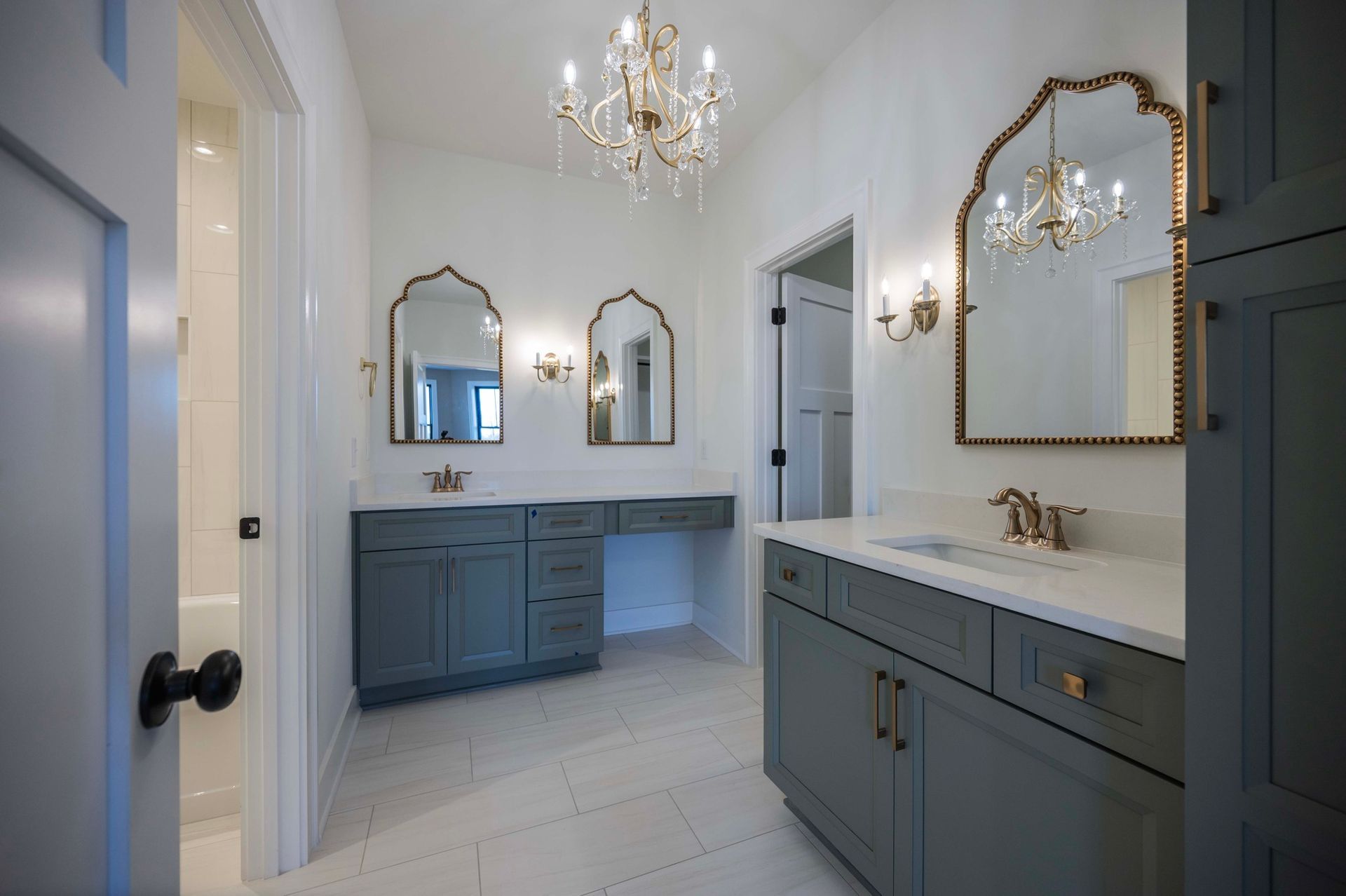 Spacious bathroom with three ornate mirrors, blue cabinets, and a chandelier.