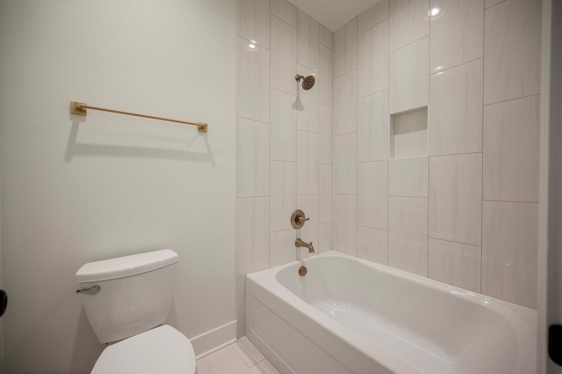 White bathroom with bathtub, toilet, gold towel rack, and tiled shower wall.