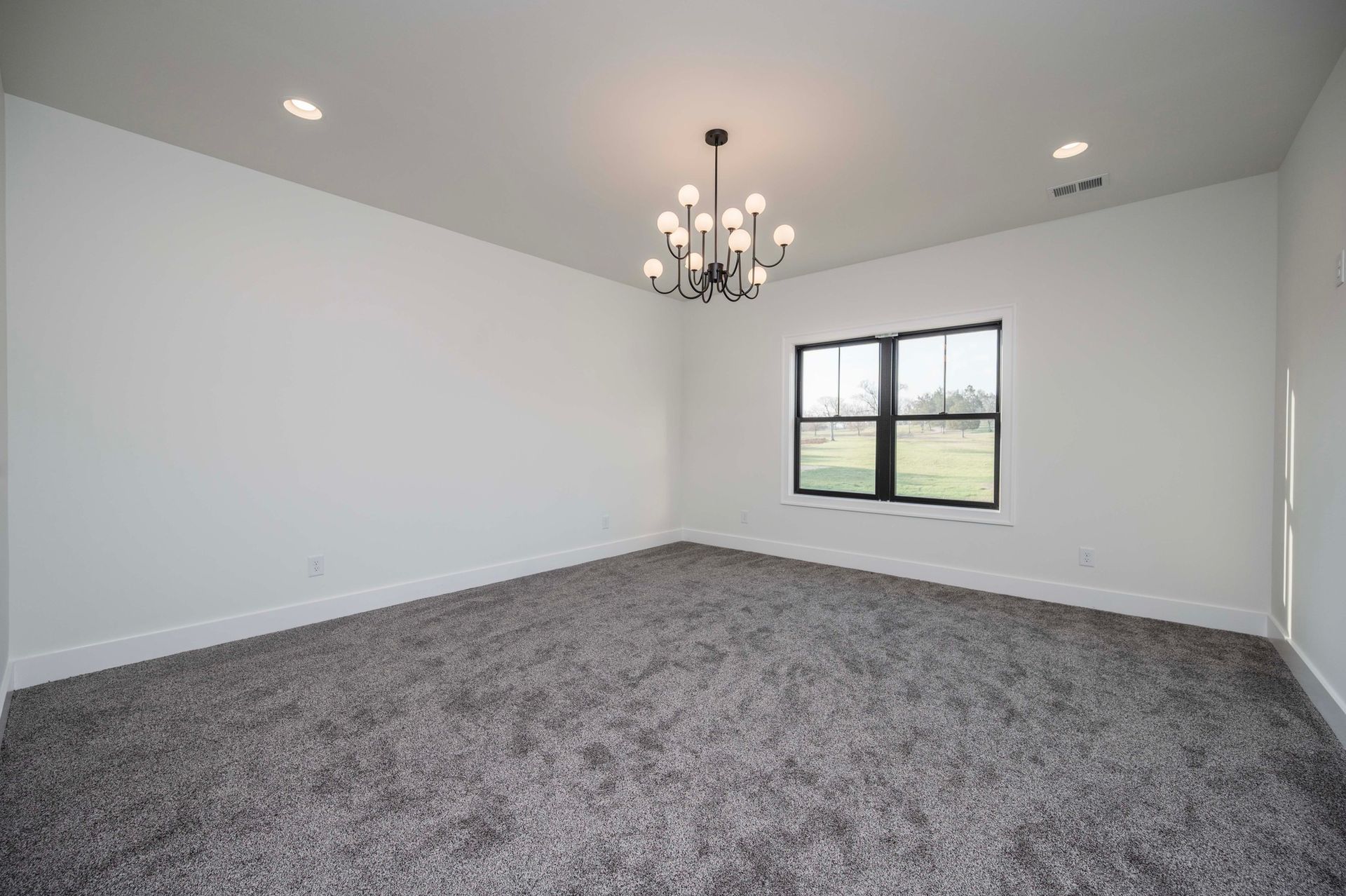 Empty room with gray carpet, white walls, black window, and a chandelier.