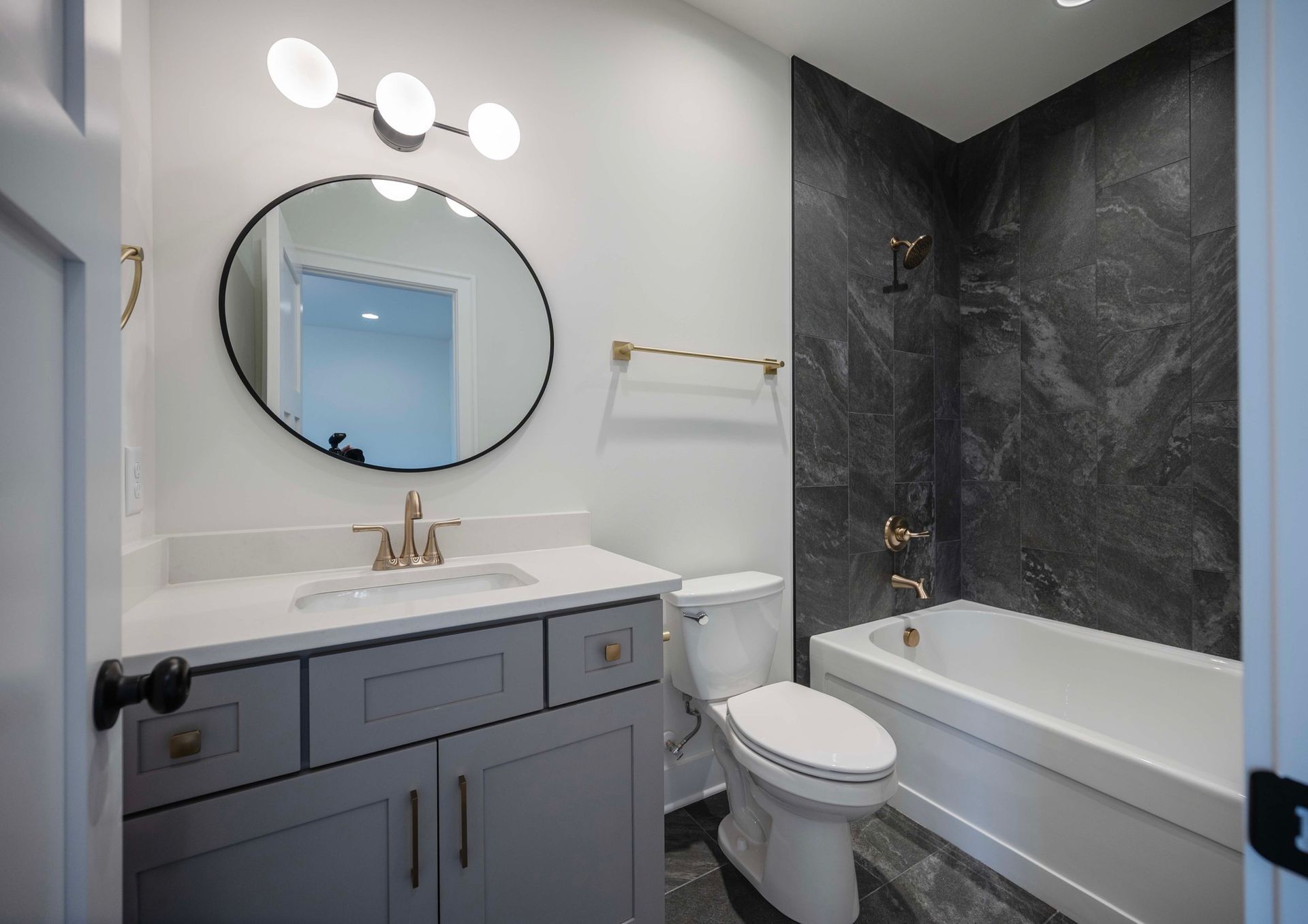Bathroom with a gray vanity, round mirror, and black accent wall.