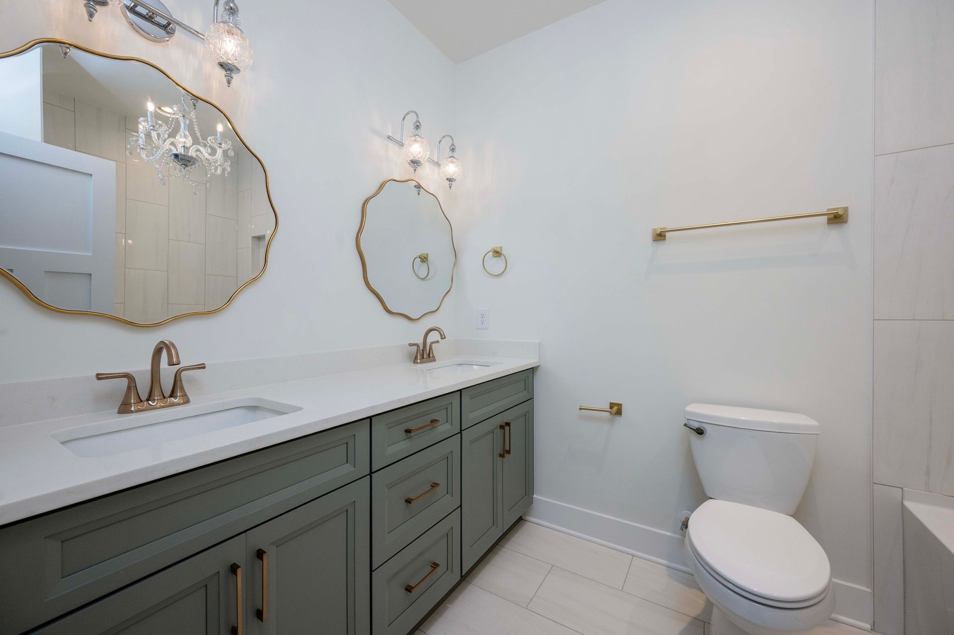 Bathroom with green vanity, gold fixtures, and two ornate mirrors. White walls and toilet.