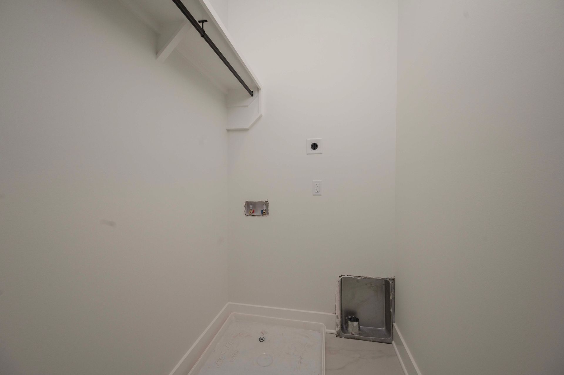 Empty, white-walled laundry room with plumbing and electrical outlets.