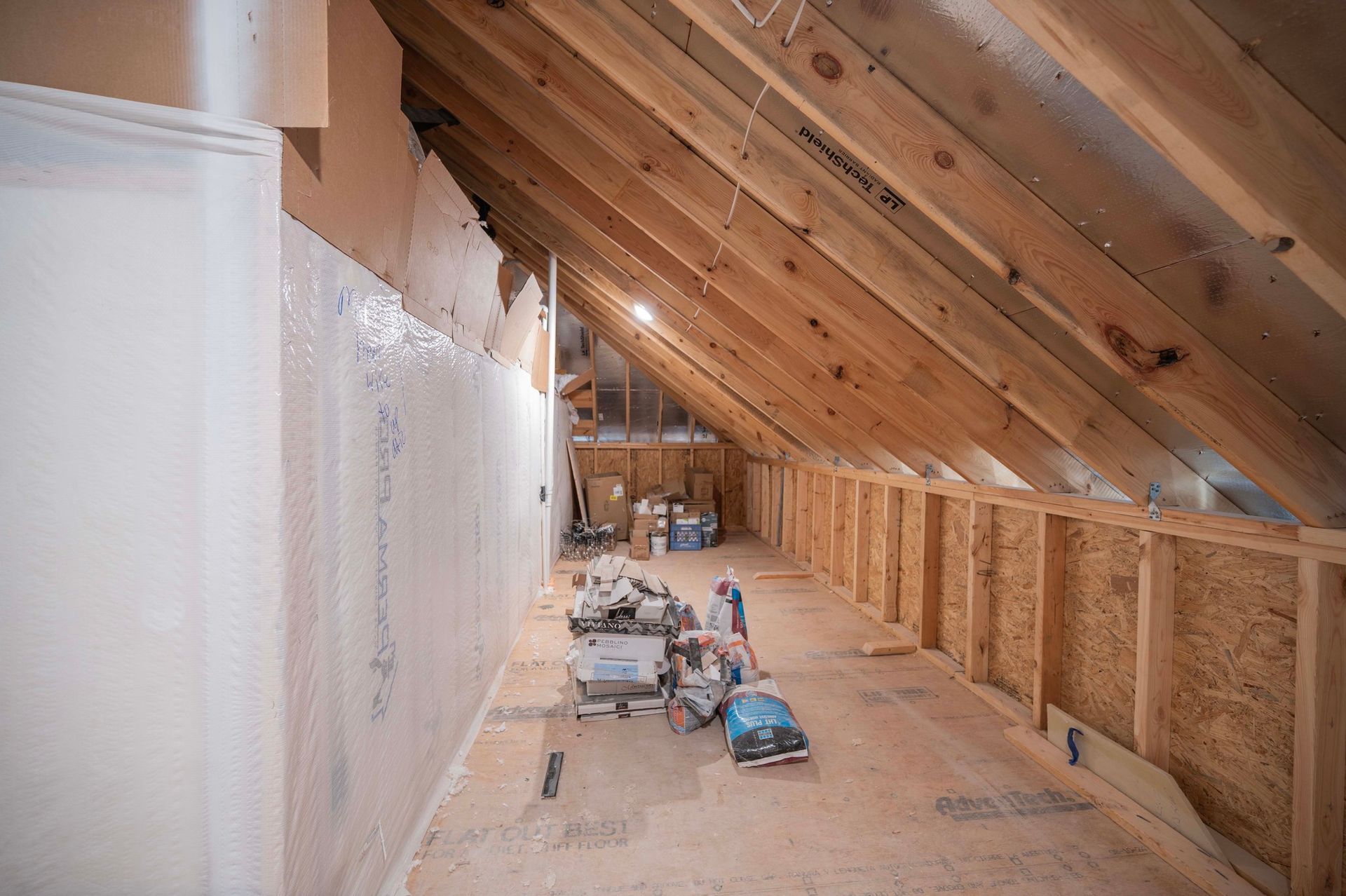Interior of unfinished attic with exposed wood beams and construction materials.