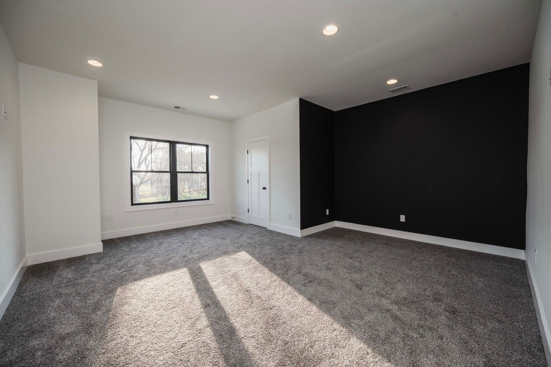 Empty room with gray carpet, black accent wall, white walls, window, and recessed lighting.