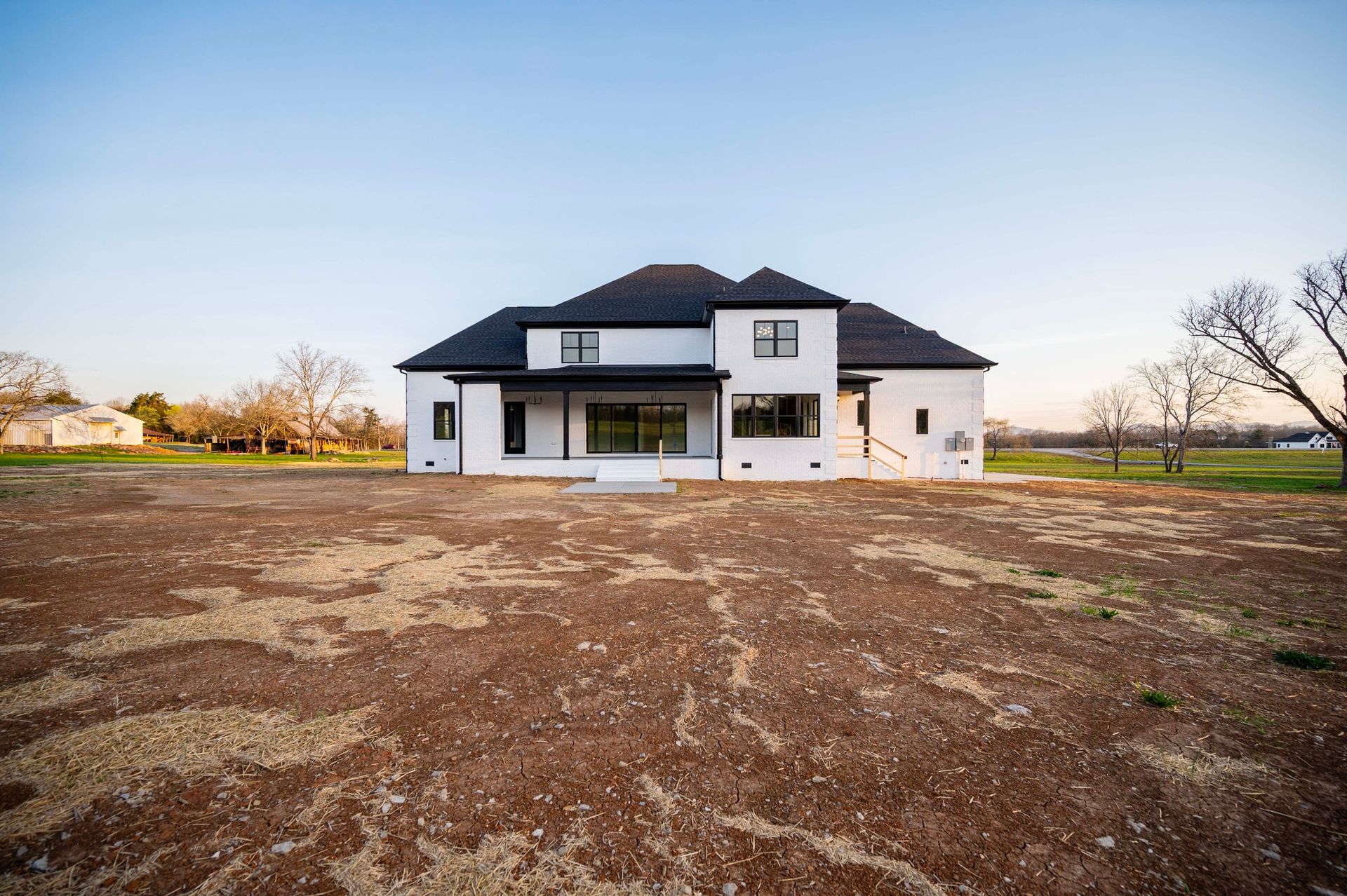 White modern house with black roof and trim, under construction in a field, with a clear sky.