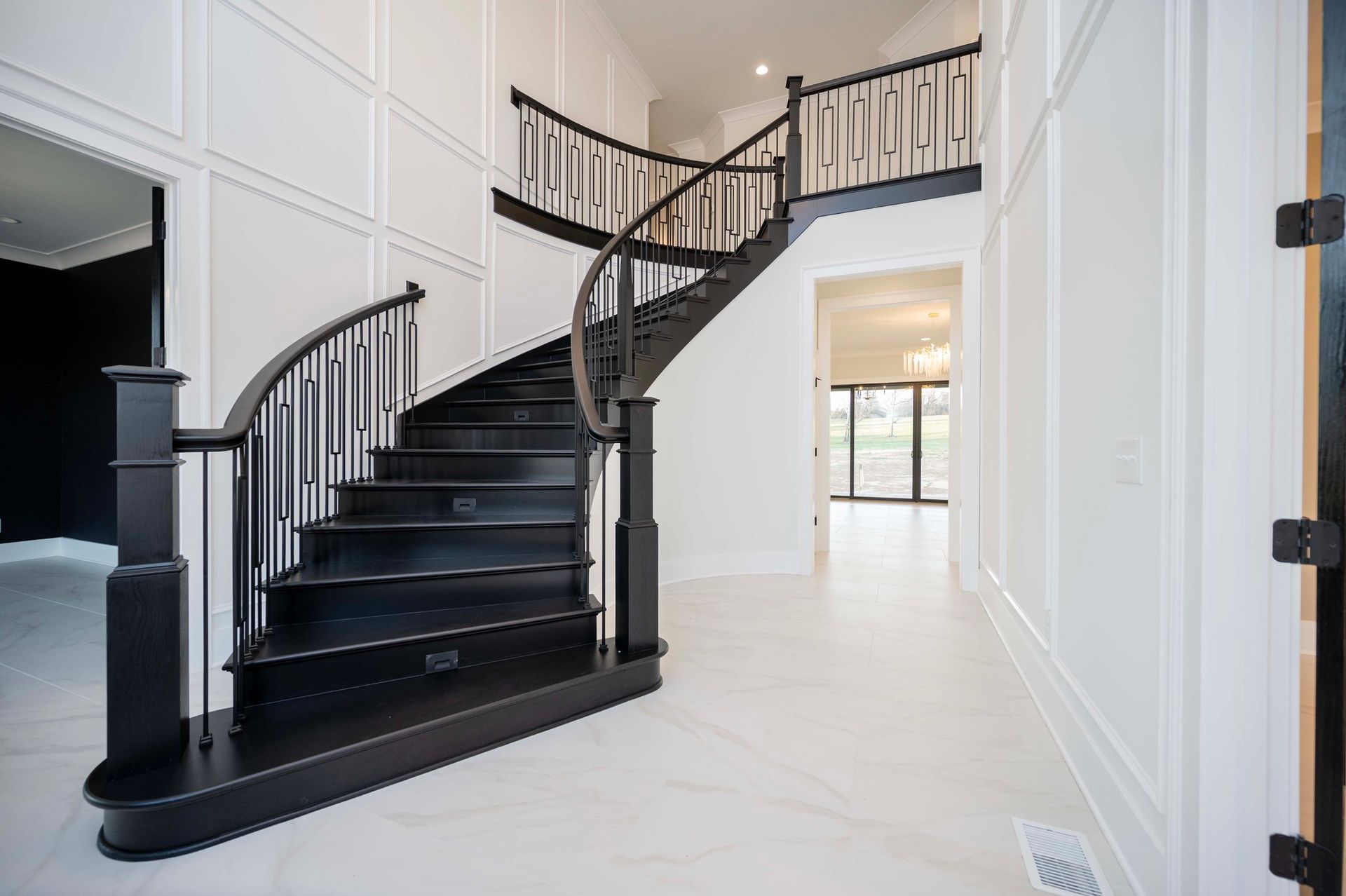 Black staircase in a bright white foyer with paneled walls and a curved banister.