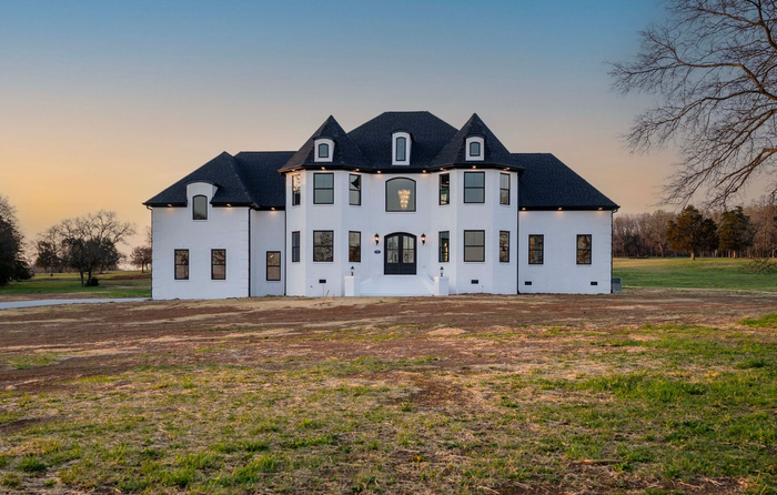 White mansion with black trim and roof in a grassy field at dusk.