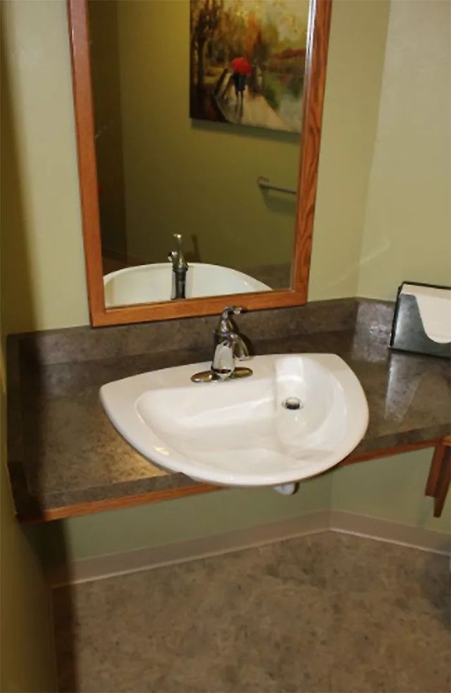 Small bathroom sink with mirror, dark countertop, and beige walls.
