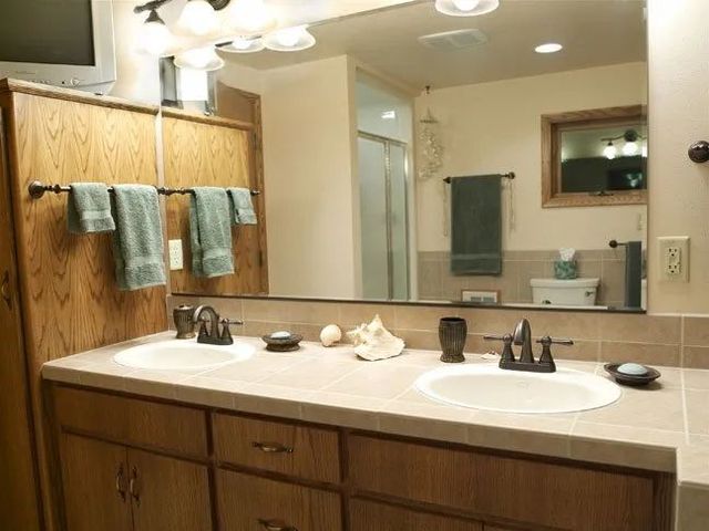Bathroom vanity with double sinks, large mirror, and towels hanging on wooden cabinets.